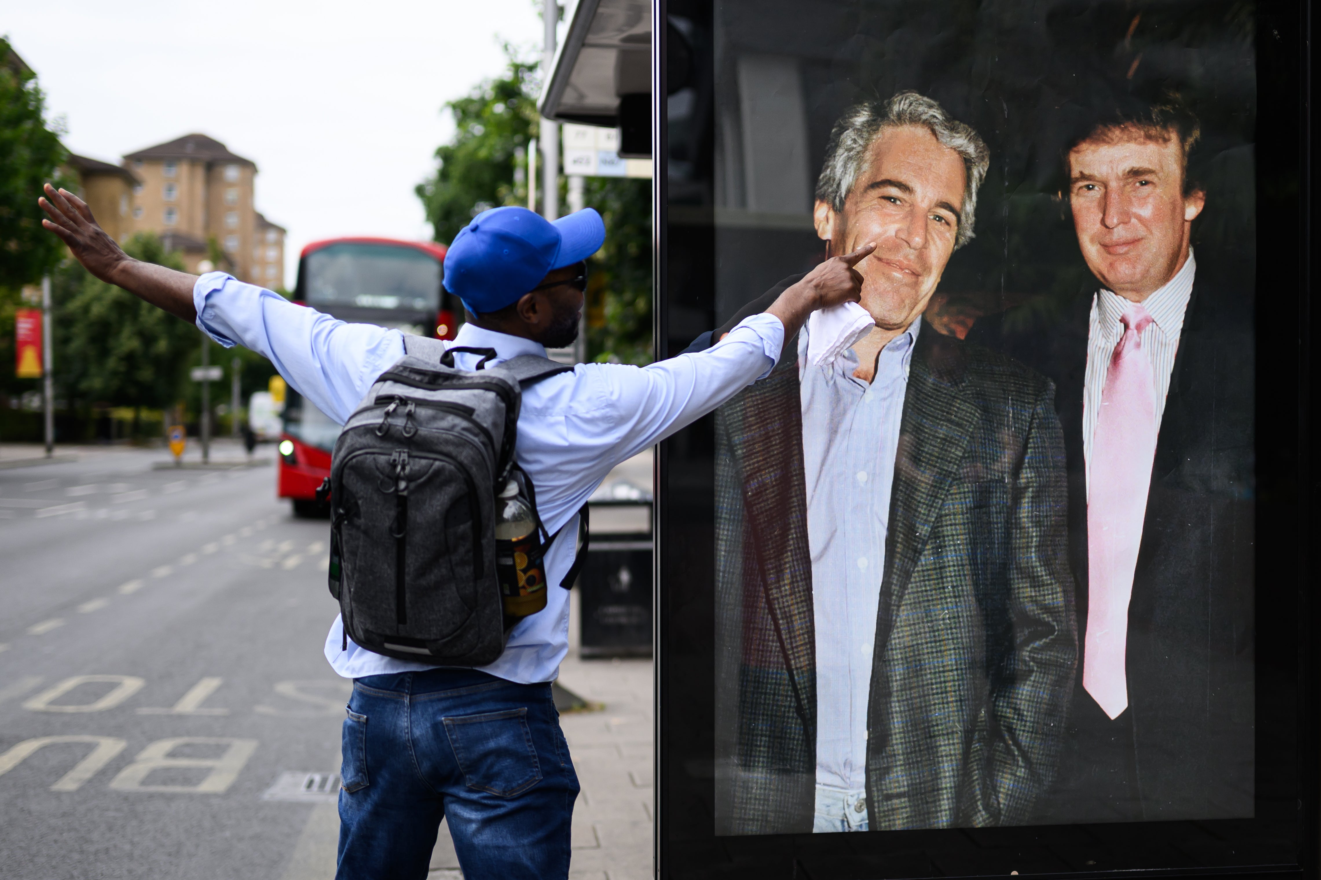 A man gestures to a photograph of US President Donald Trump and convicted child sex offender Jeffrey Epstein after it is unofficially installed in a bus shelter on July 17, 2025 in London, England