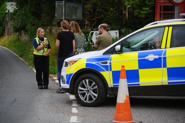 Police talk to people near the scene of the coach crash on the A396 Cutcombe Hill (Ben Birchall/PA)