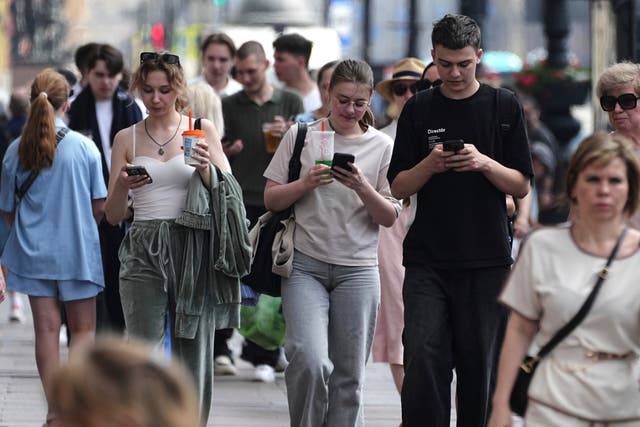 <p>Pedestrians look at their phones while walking through St. Petersburg, Russia</p>