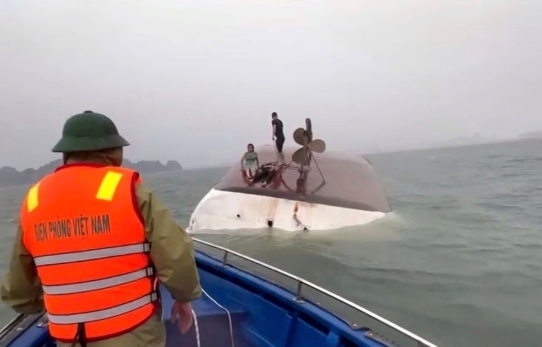Survivors sit on top of the capsized vessel as rescue workers arrive