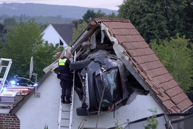 <p>A police officer checks a car stuck in the wall of a barn following an accident in Bohmte, Germany</p>