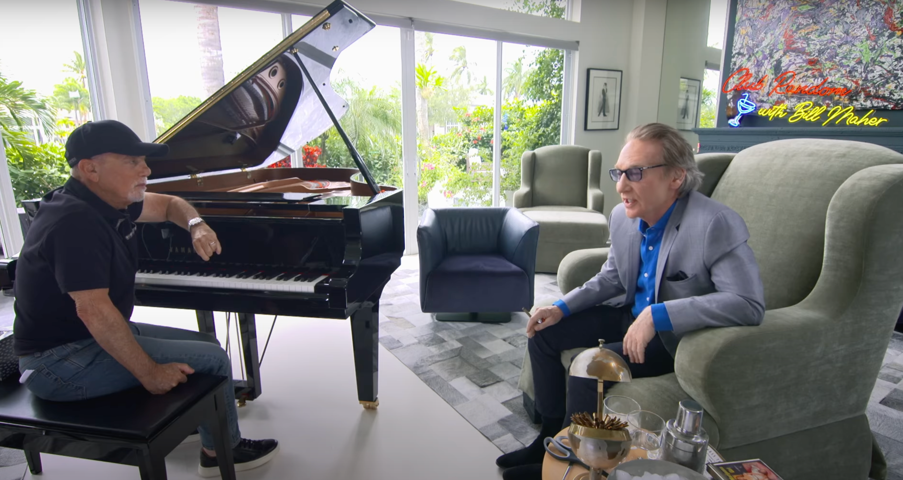 Billy Joel (left) sits at the piano during an interview with Bill Maher (right) for his 'Club Random' podcast
