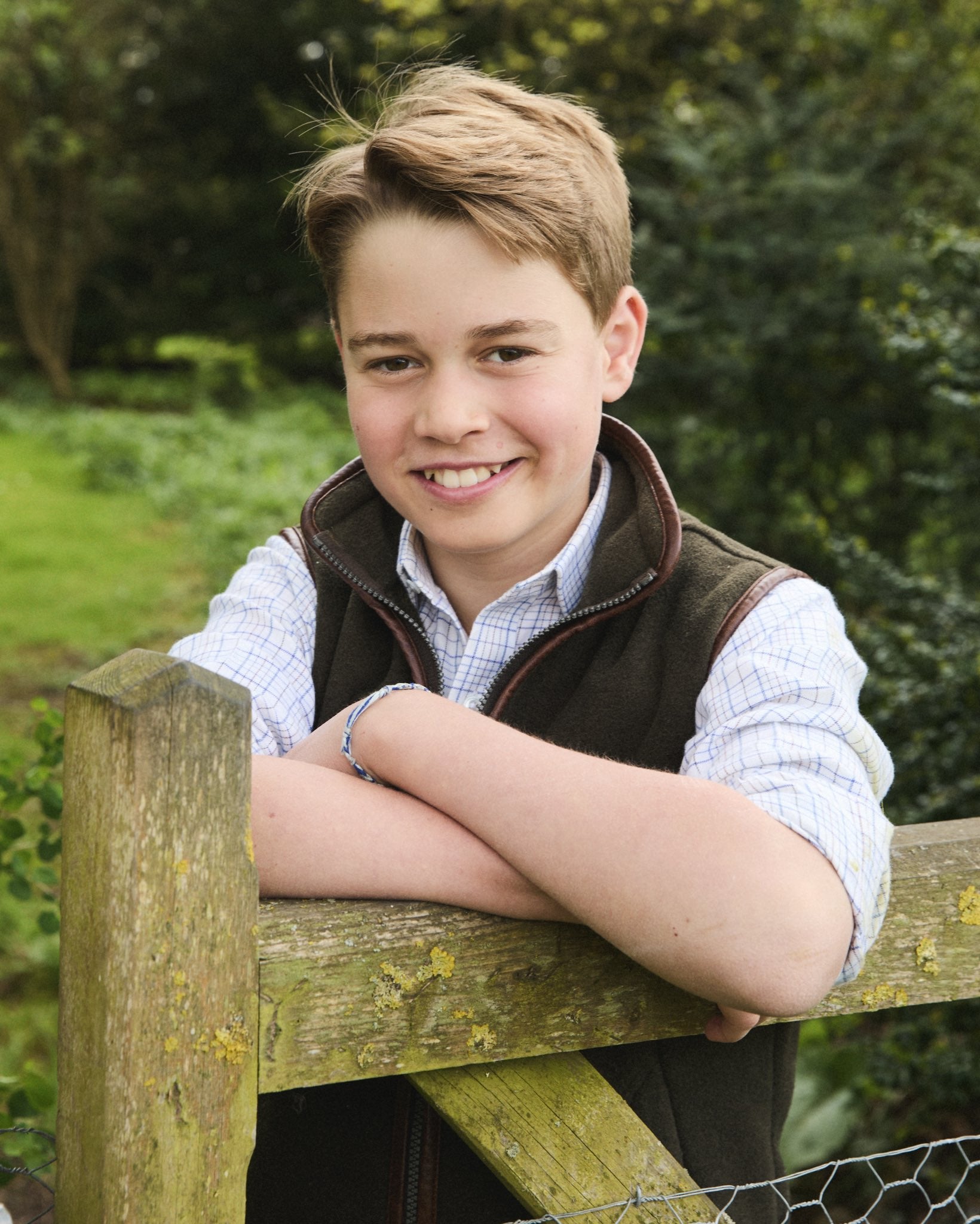 George is wearing a white checked shirt with rolled up sleeves and a dark green fleece gilet
