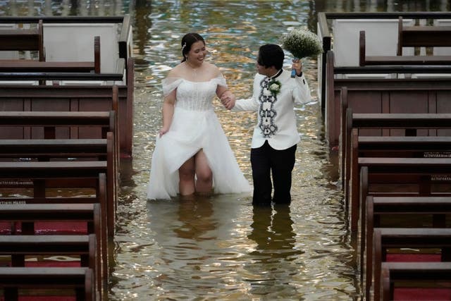 <p>Newlyweds Jade Rick Verdillo (right) and Jamaica  Aguilar walk hand in hand during their wedding at the flooded Barasoain church in Malolos, Bulacan province, Philippines on Tuesday, 22 July 2025</p>