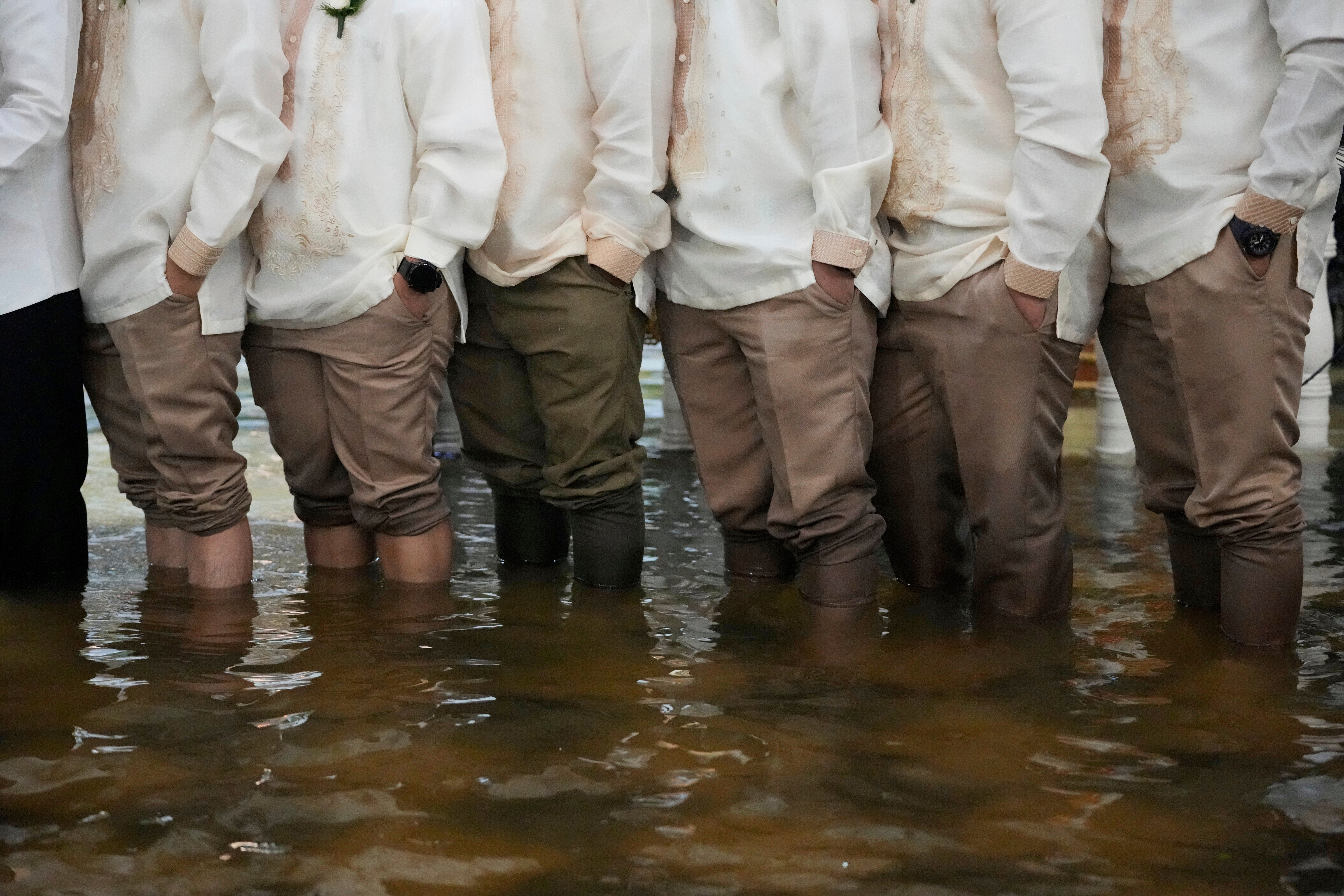 Groomsmen and guests stand knee deep in floodwaters wearing the traditional Barong Tagalog at Barasoain church in Malolos, Bulacan province, Philippines
