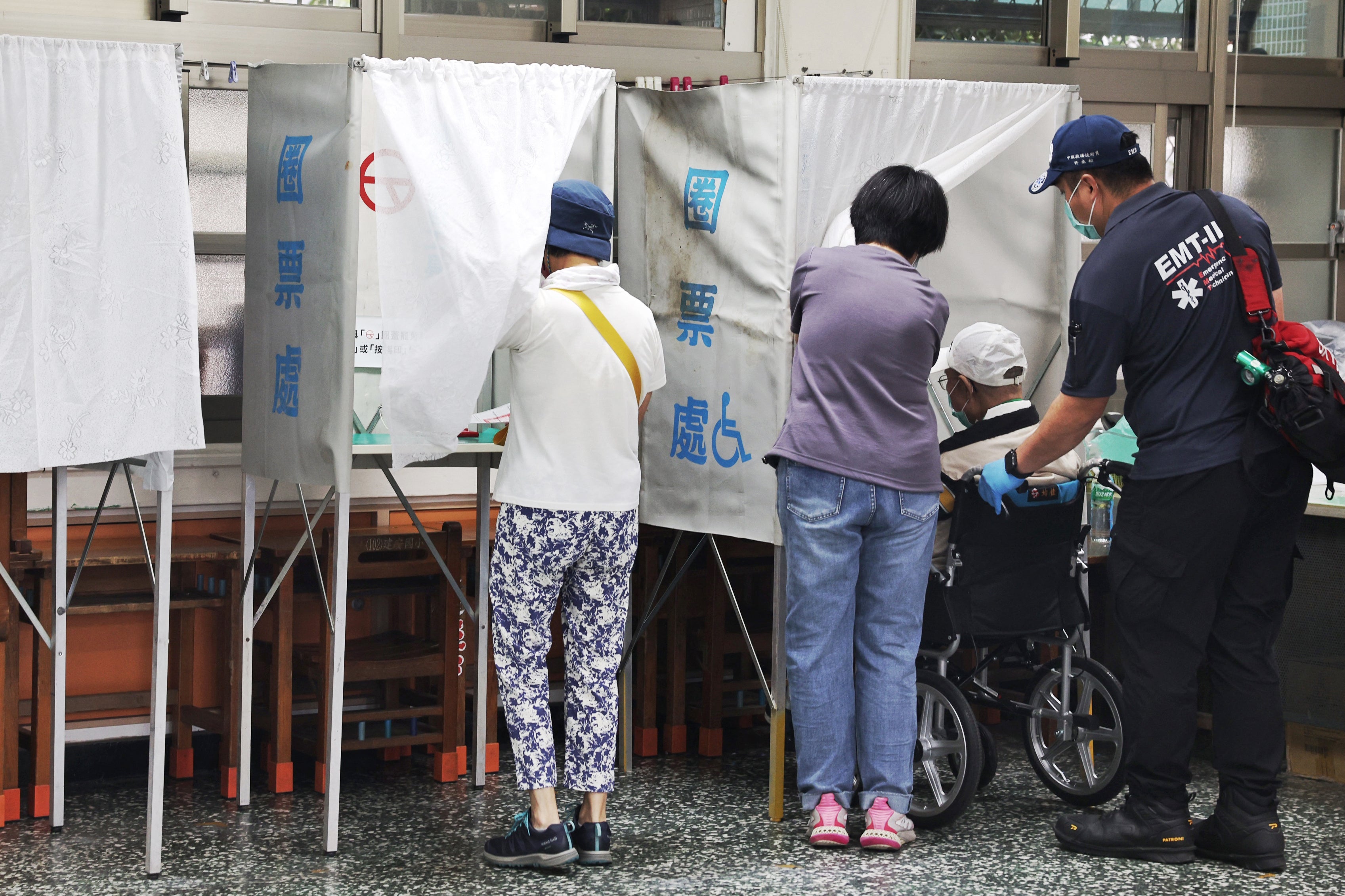 A voter on a wheelchair (2nd R) is brought to a booth after arriving at a polling station by ambulance to vote in the recall election in Taipei on July 26, 2025