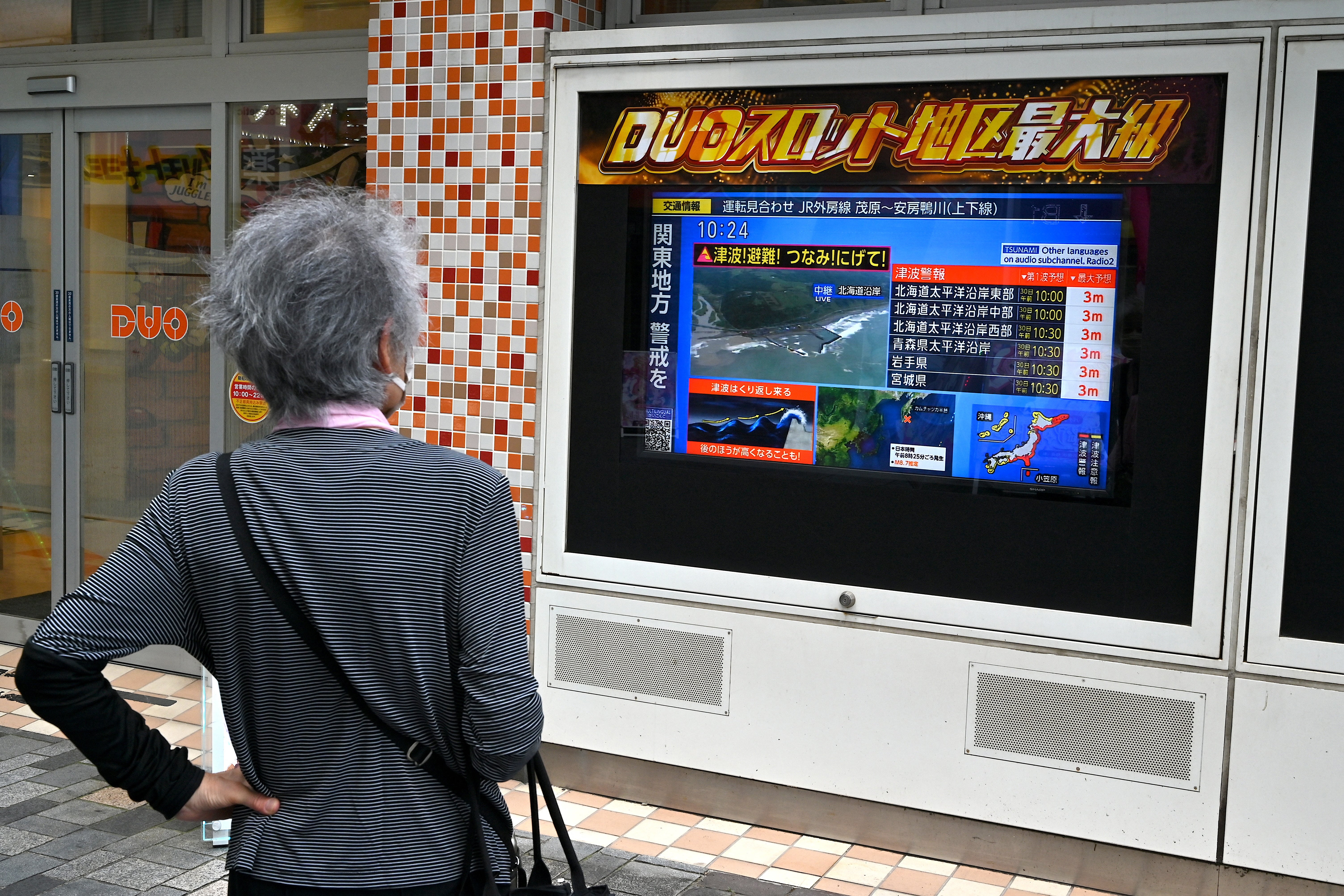 A woman watches a television broadcast of a tsunami warning for much of coastal Japan following an 8.8 magnitude quake in the sea off eastern Russia, outside a gaming shop in central Tokyo on 30 July 2025