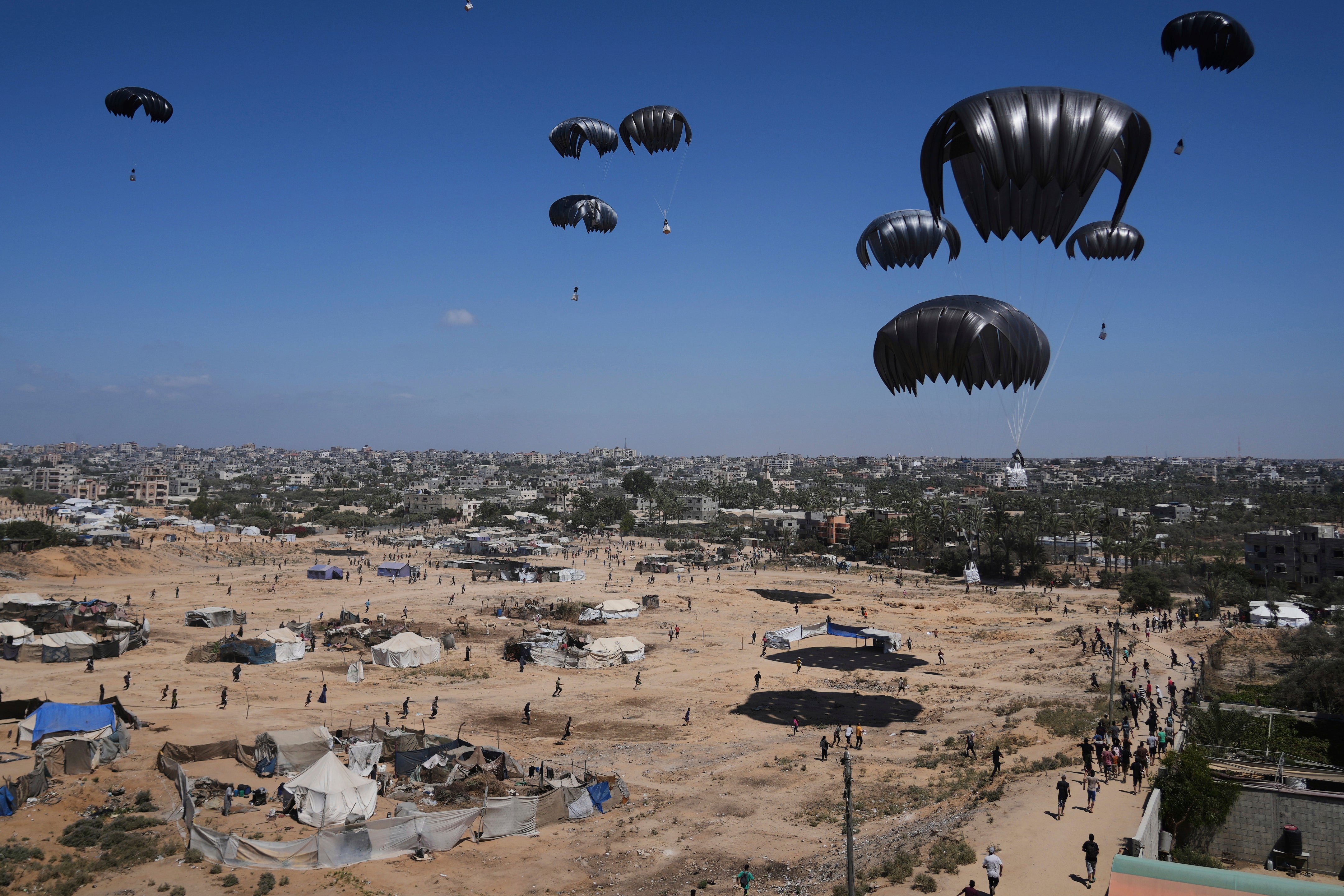 Palestinians rush to collect humanitarian aid airdropped by parachutes into Zawaida in the central Gaza Strip