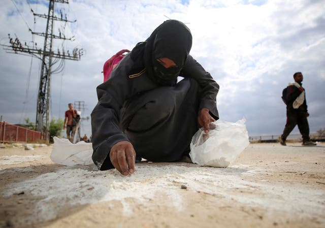 <p>A woman collects flour from the ground as Palestinians receive aid supplies from the US-backed Gaza Humanitarian Foundation</p>