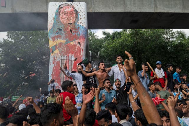 <p>Protesters beside a defaced portrait of Prime Minister Sheikh Hasina after news of her resignation, in Dhaka</p>