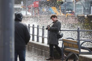A man taking pictures turns his back on the waves crushing over the esplanade