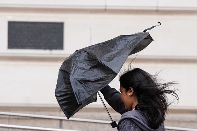 A woman struggles with her umbrella during windy conditions (Jacob King/PA)