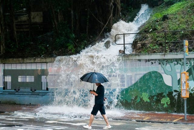 <p>A pedestrian walks past an overflowing hillside drain spilling water onto a street in the Quarry Bay area of Hong Kong on 5 August 2025</p>