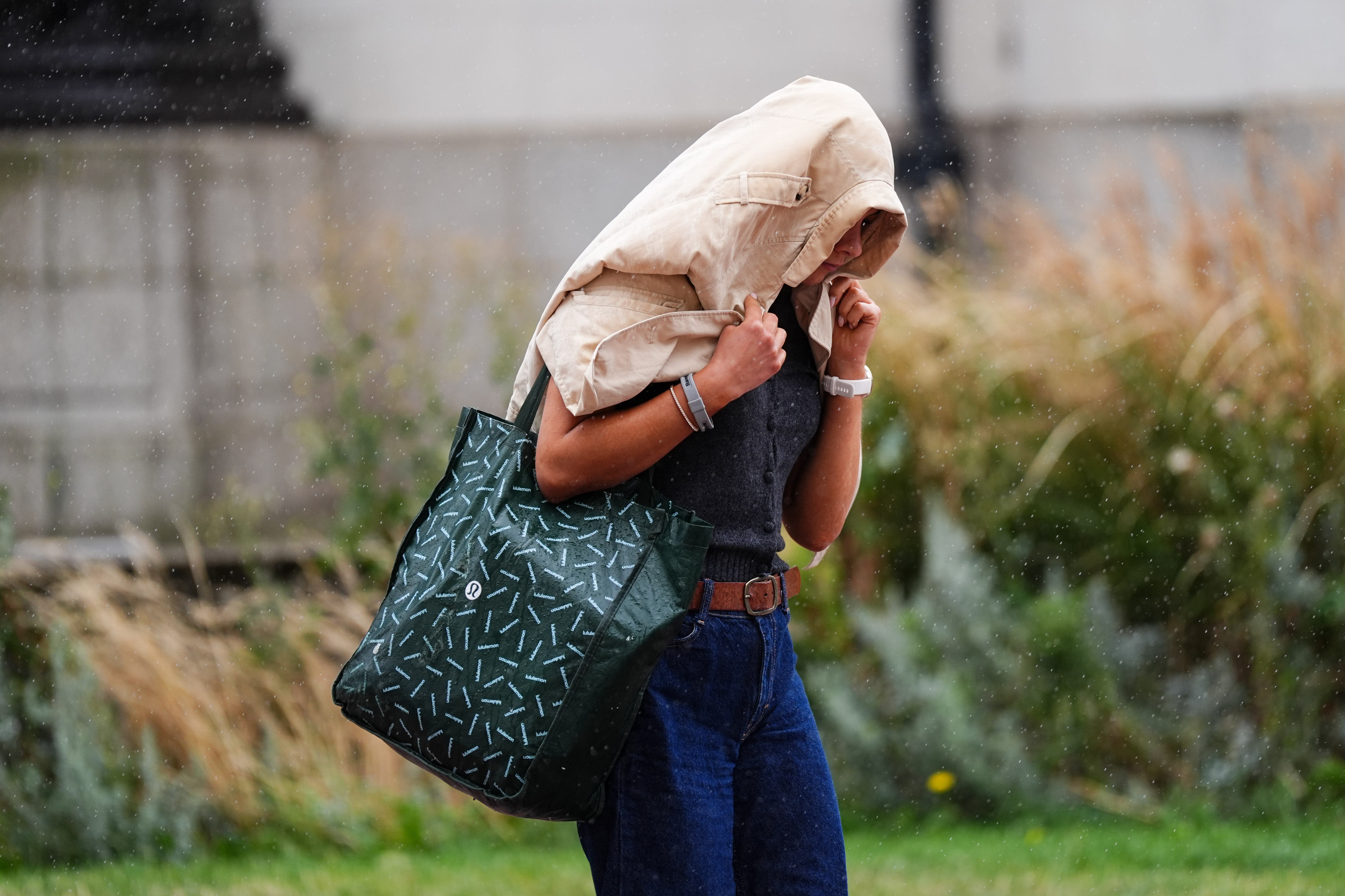 A woman uses a coat to cover themselves from rainfall in Birmingham during Storm Floris (Jacob King/PA)