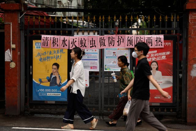 <p>Residents walk past a sign in Guangzhou which reads: "Let's work together to clear stagnant water and eliminate mosquito breeding"</p>
