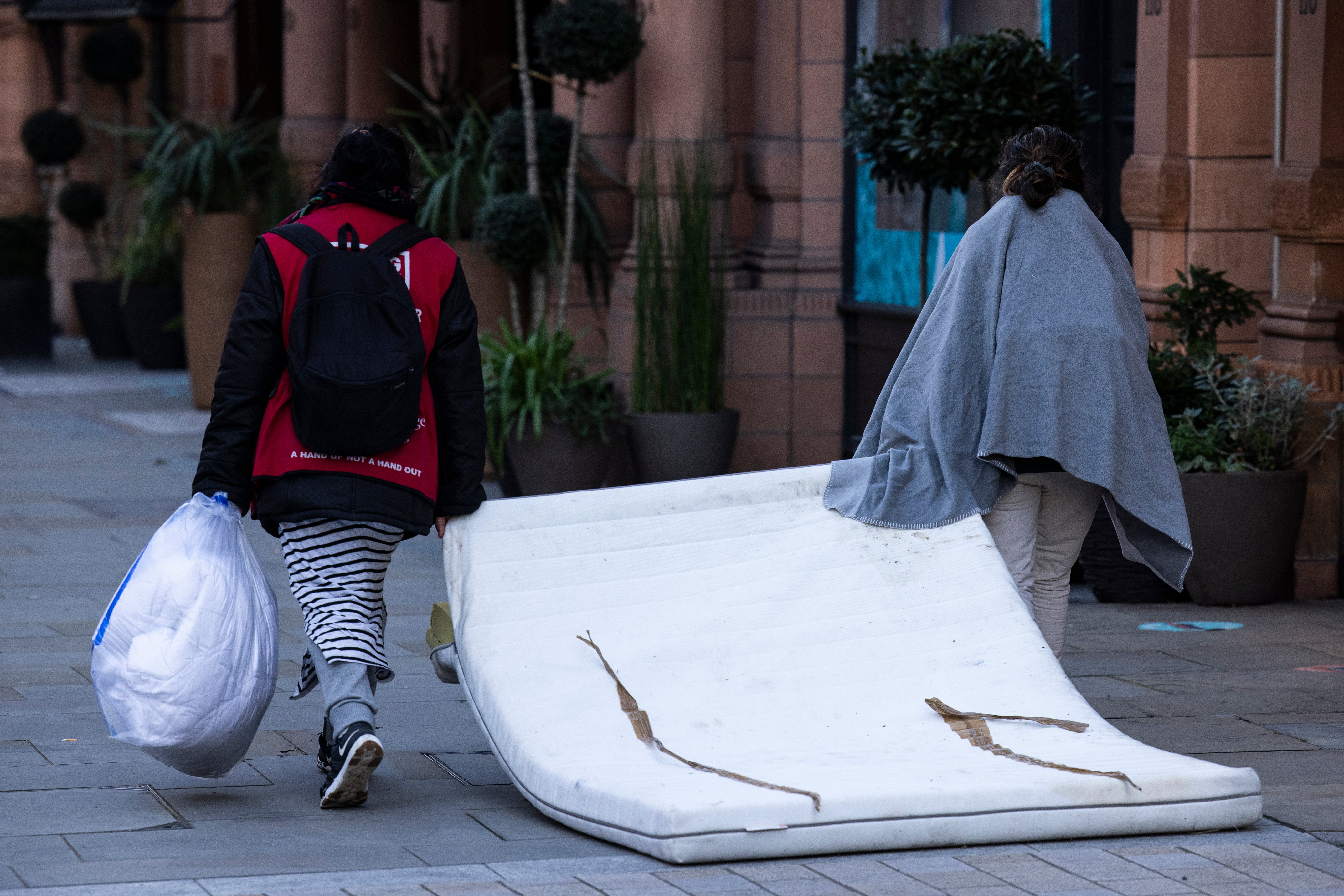 <p>Two rough sleepers drag a mattress down the road in London’s Mayfair</p>