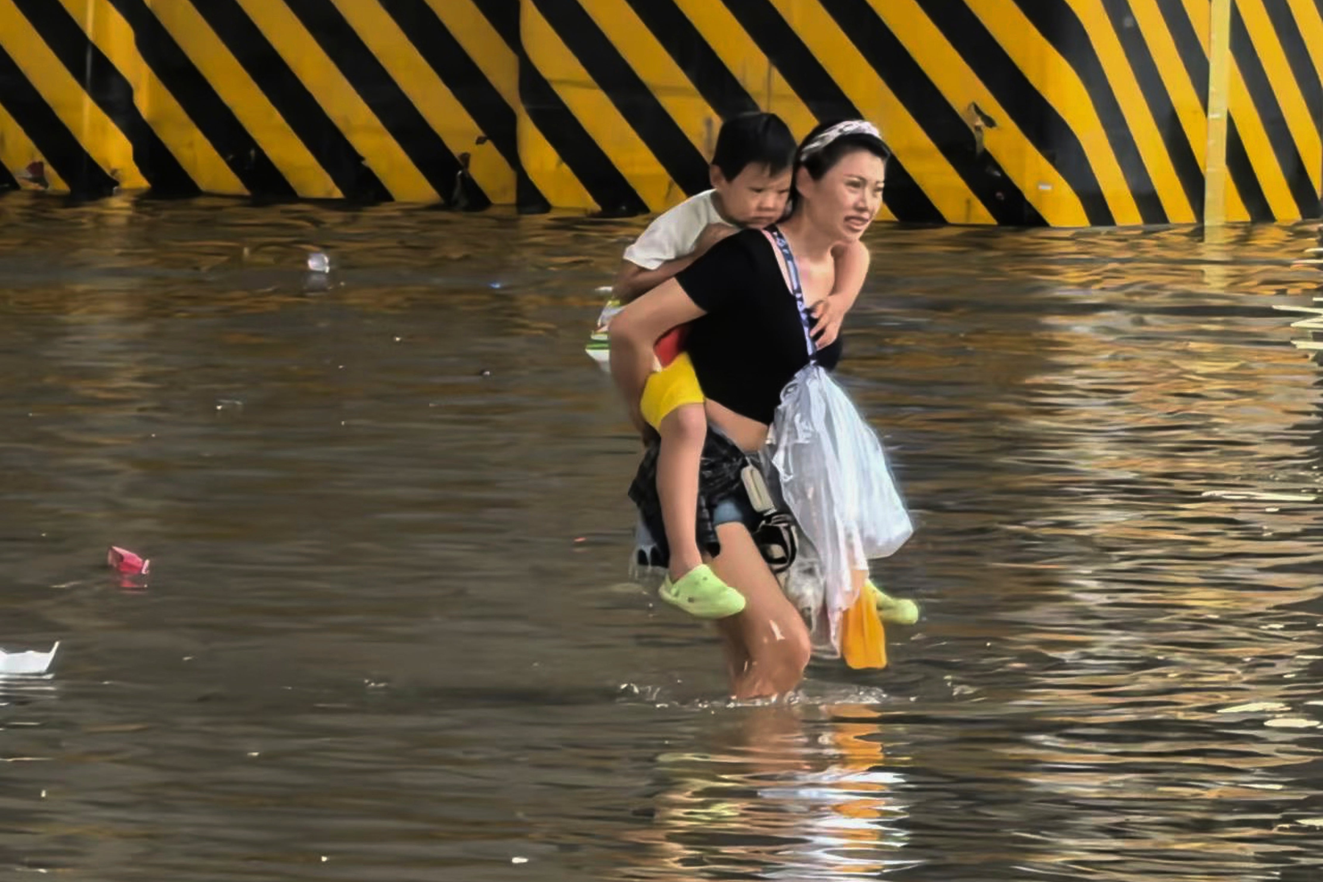 A woman carrying a child wades through a flooded road in Zhengzhou in China's Henan province