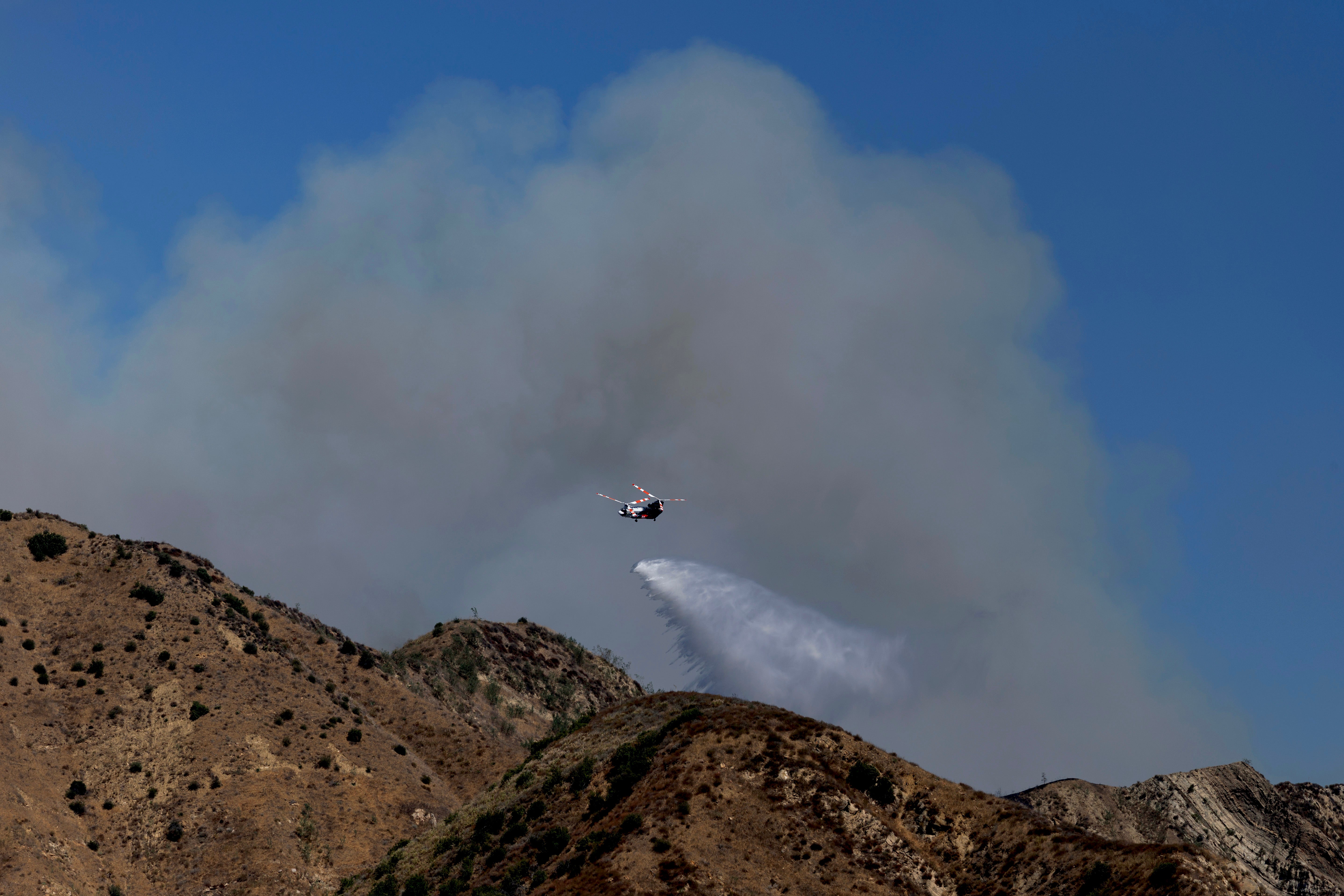 A helicopter drops water on a hillside during the Canyon Fire on August 7 in Piru, California