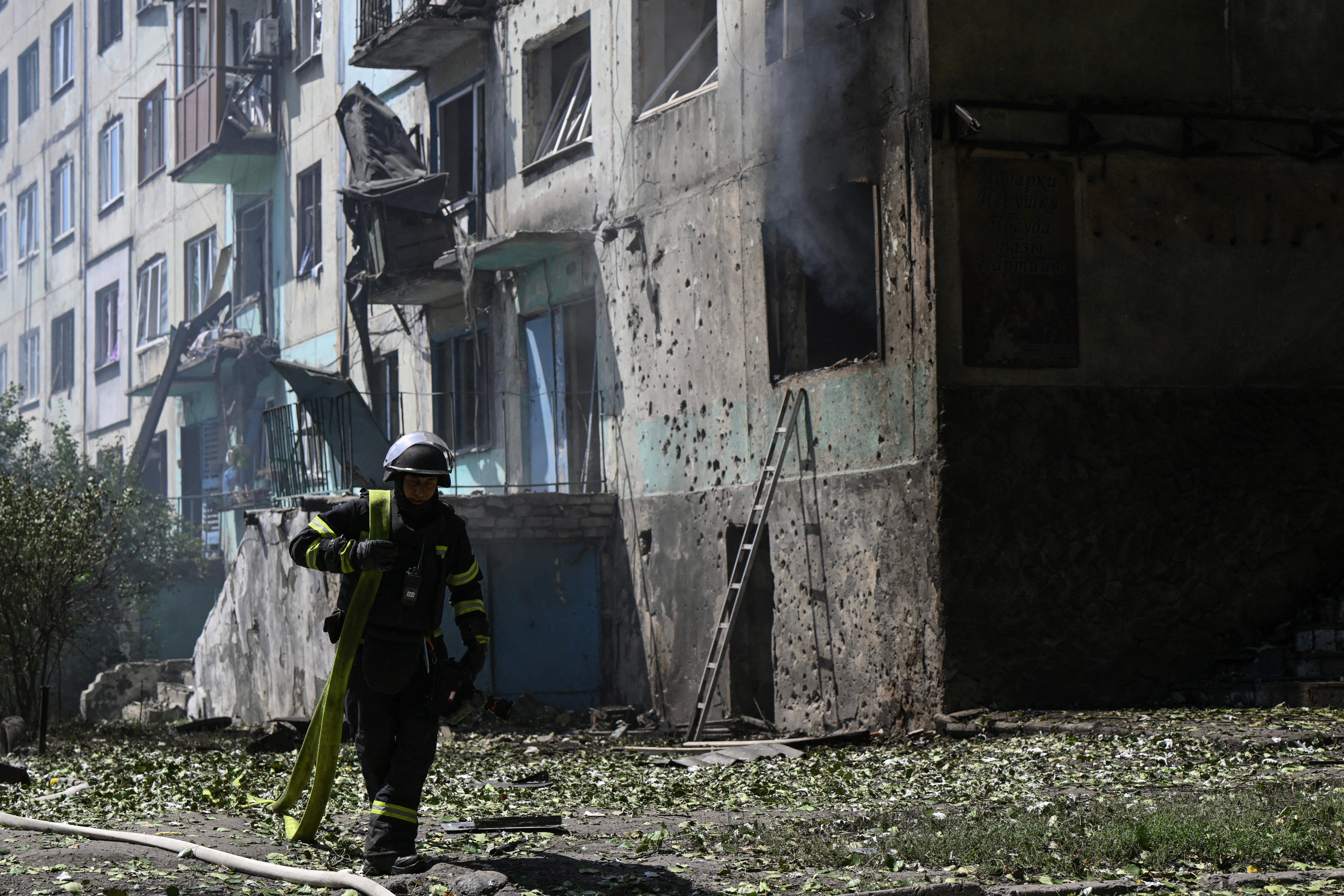 An Ukrainian firefighter carries a water pump to extinguish fire in a residential building at the site of a Russian drone strike in the town of Bilozerske in the Donetsk region on Sunday