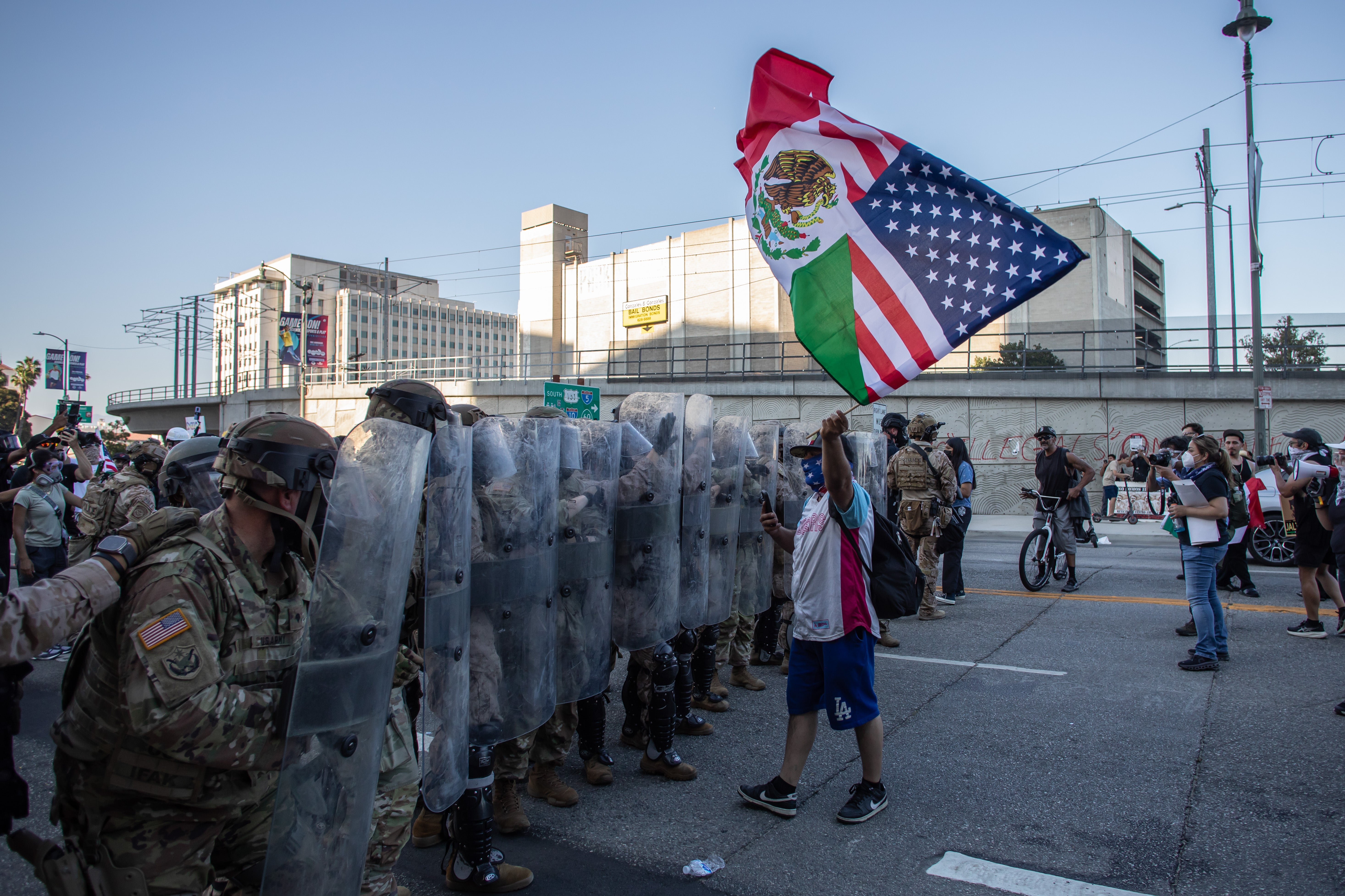 A demonstrator lifts an American-Mexican flag in front of Marines while they stand guard during a protest against ICE raids on July 4 in Los Angeles