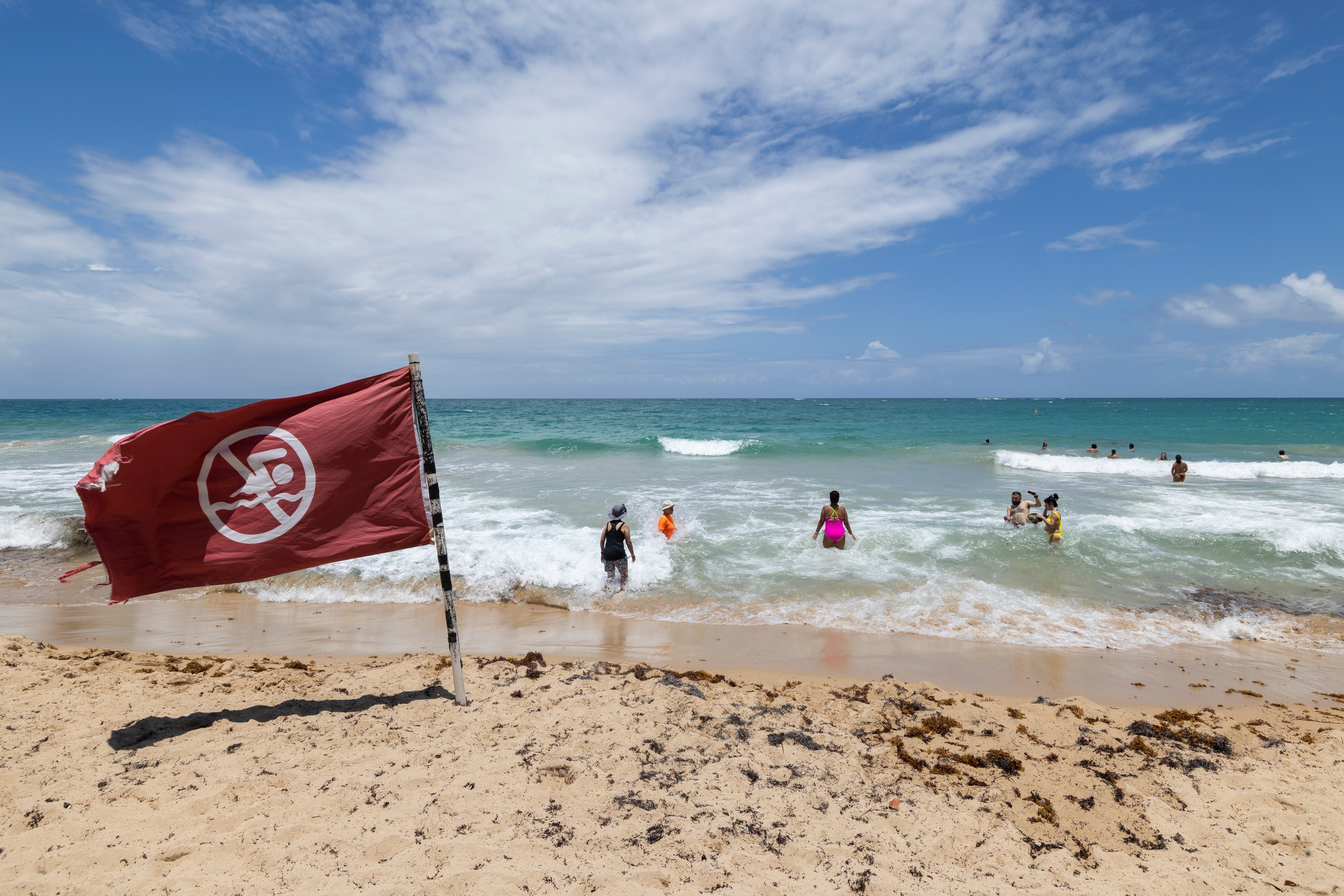 A warning flag flies on the beach as people swim in Condado, Puerto Rico, as Hurricane Erin approaches, Friday, Aug. 15, 2025. (AP Photo/Alejandro Granadillo)