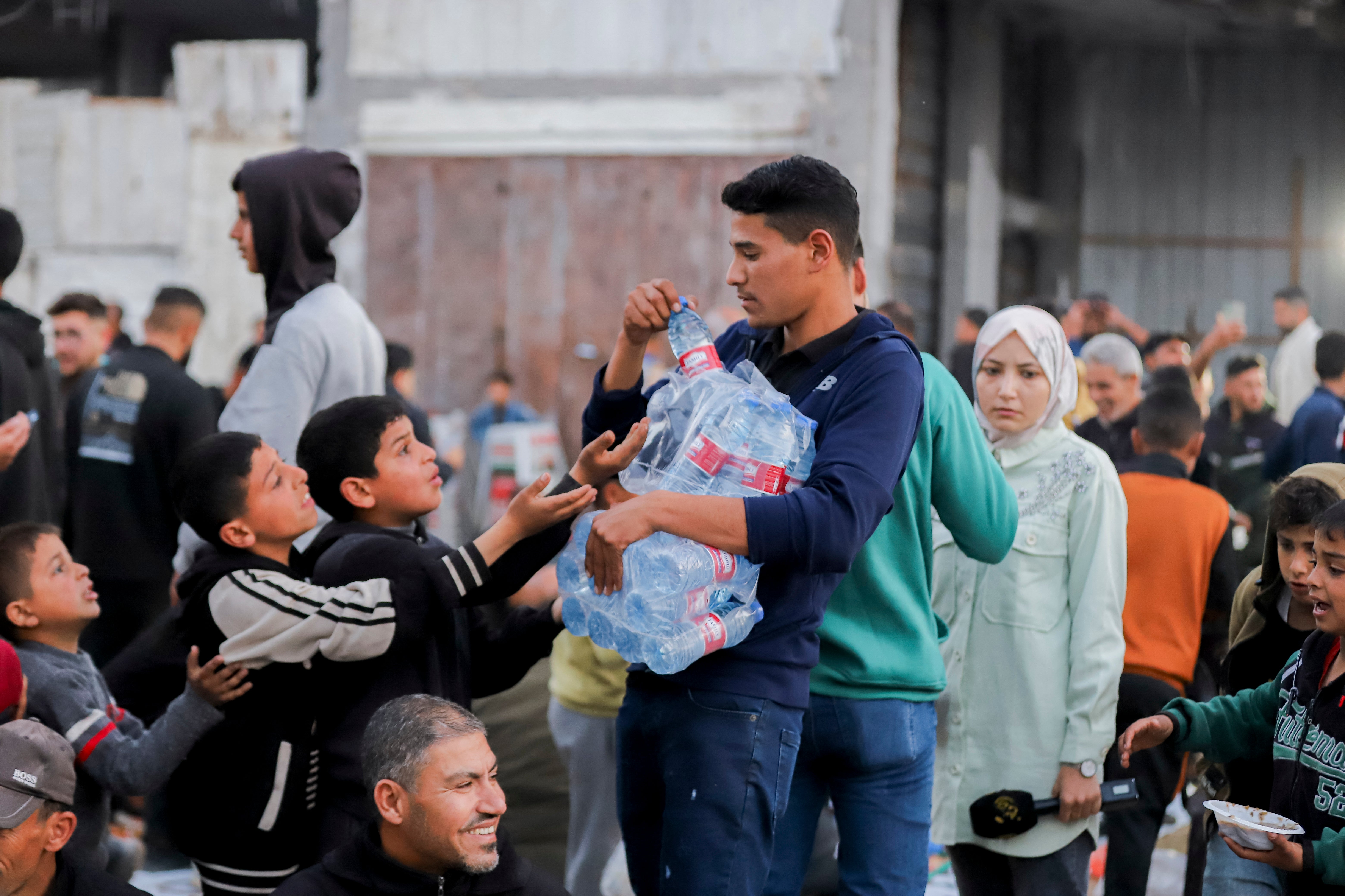 A young man distributes bottled water to children during Iftar in Beit Lahia, northern Gaza