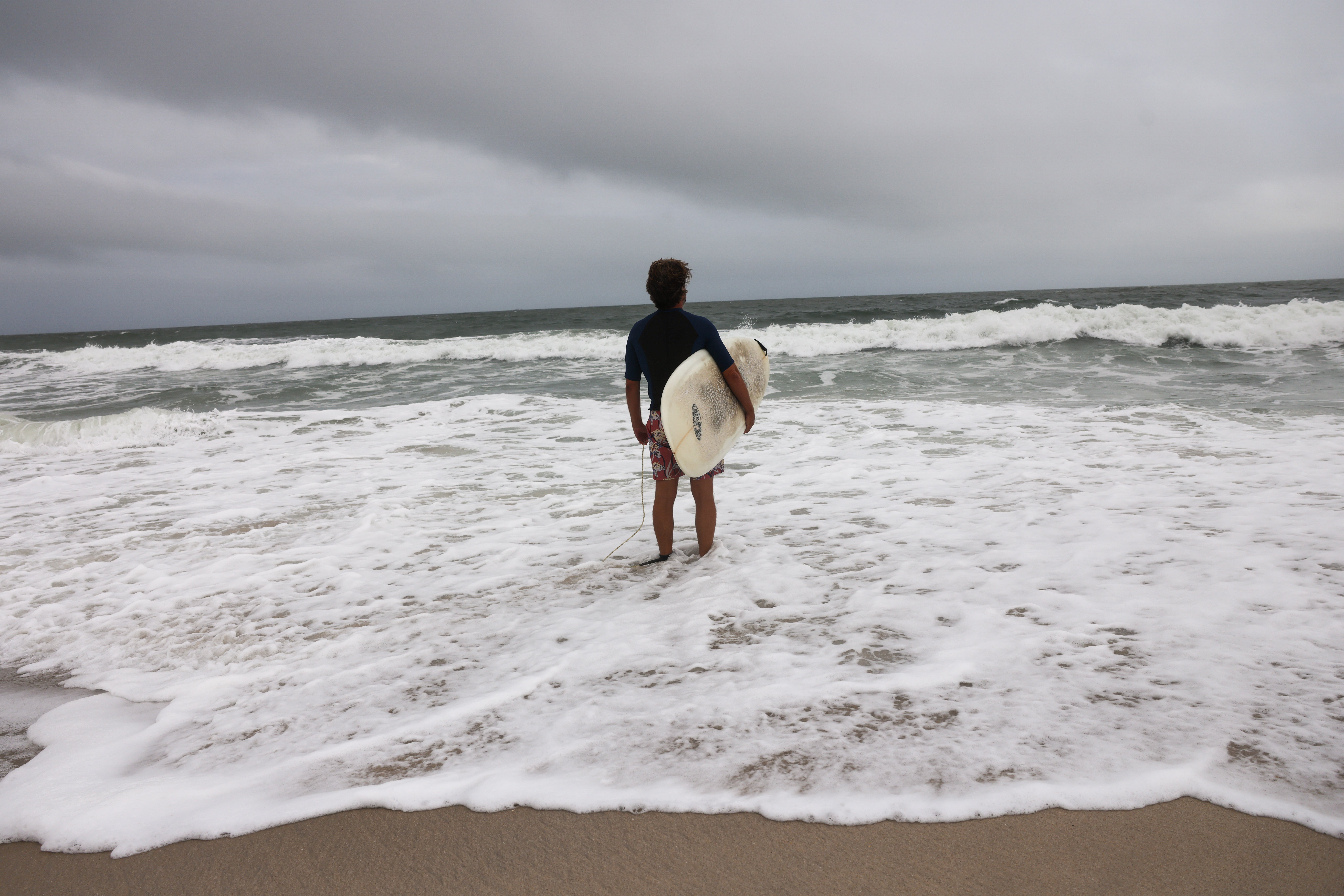 A surfer prepares to go into the ocean on a beach closed to swimmers — there's always one