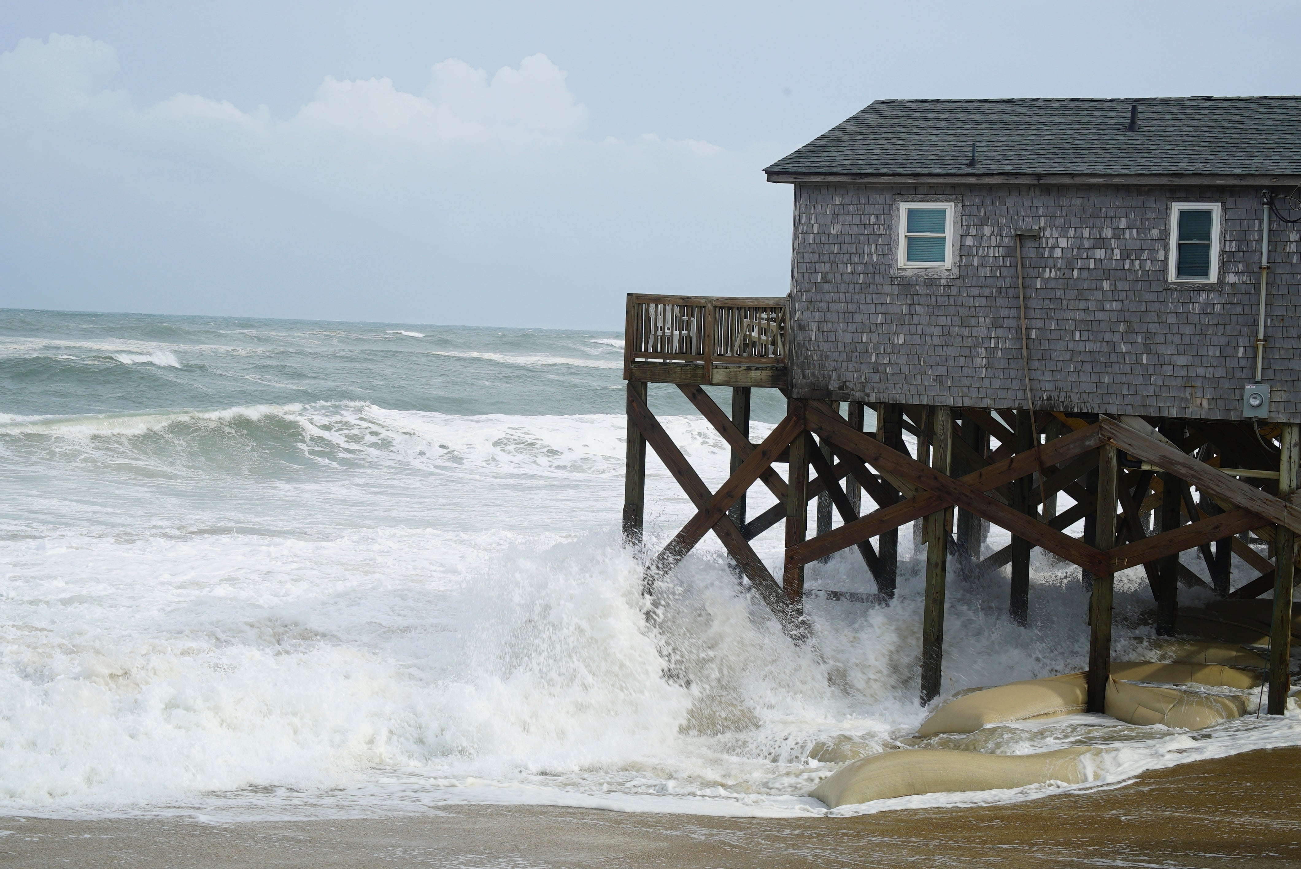 Waves driven by Erin crash against the sandbagged pilings of a building in Buxton, North Carolina, on Wednesday
