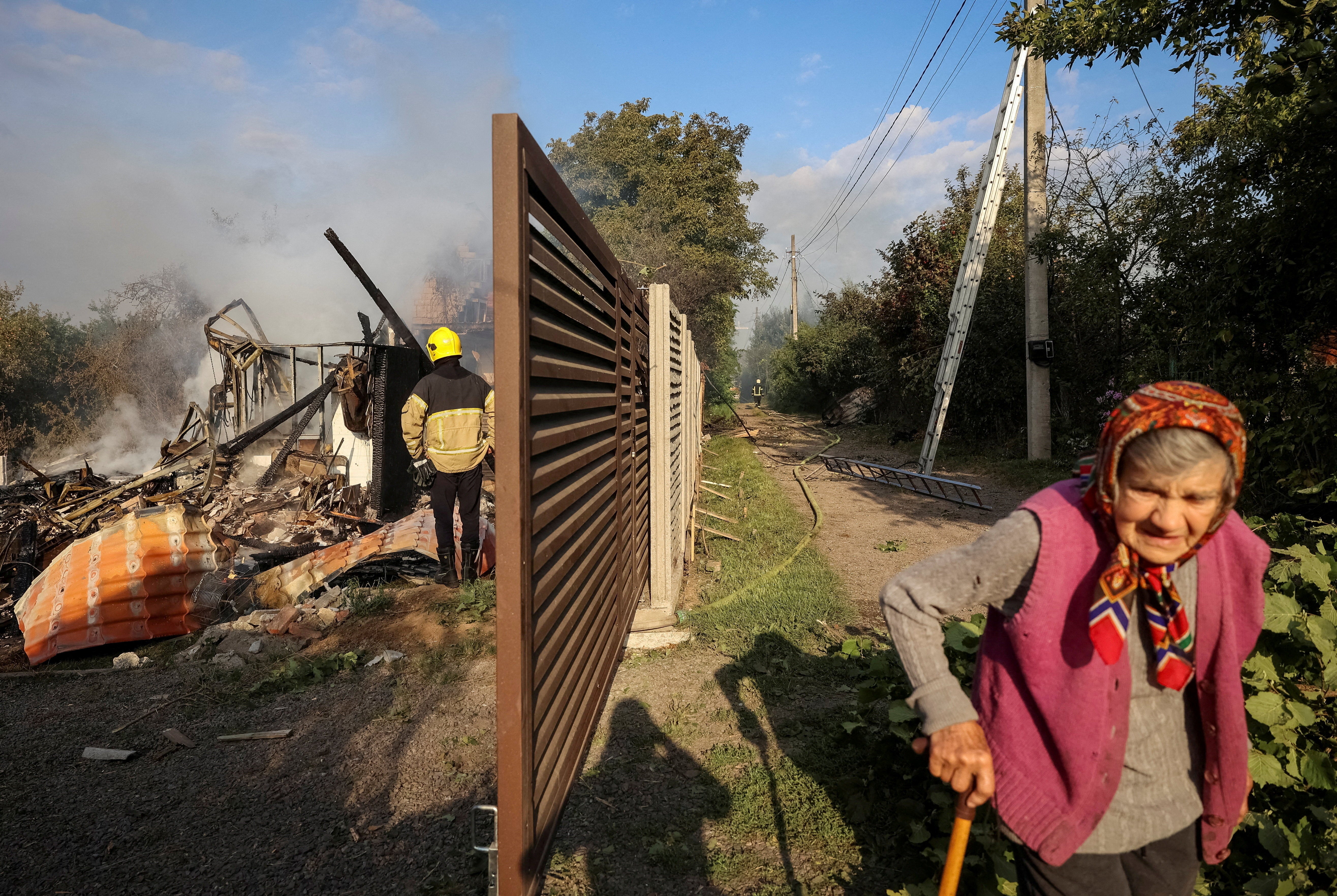 A resident walks along a street as a firefighter works at the site of a Russian missile strike, amid Russia's attack on Ukraine, in the village of Sknyliv on the outskirts of Lviv