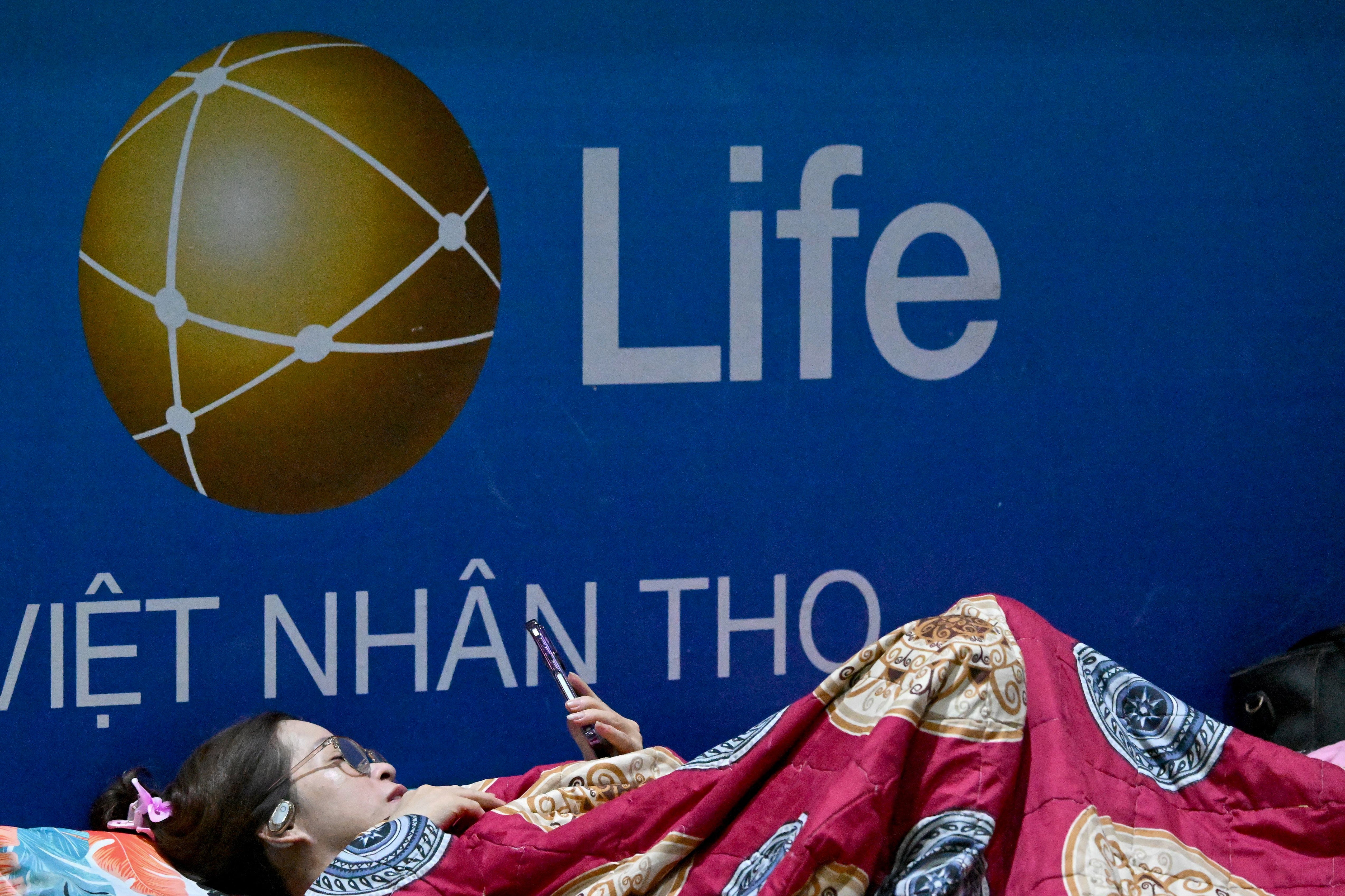 A woman uses her phone as she takes shelter inside the Nghe An Provincial Gymnasium in Vinh city, Nghe An province, on 25 August 2025, before Typhoon Kajiki makes landfall in Vietnam