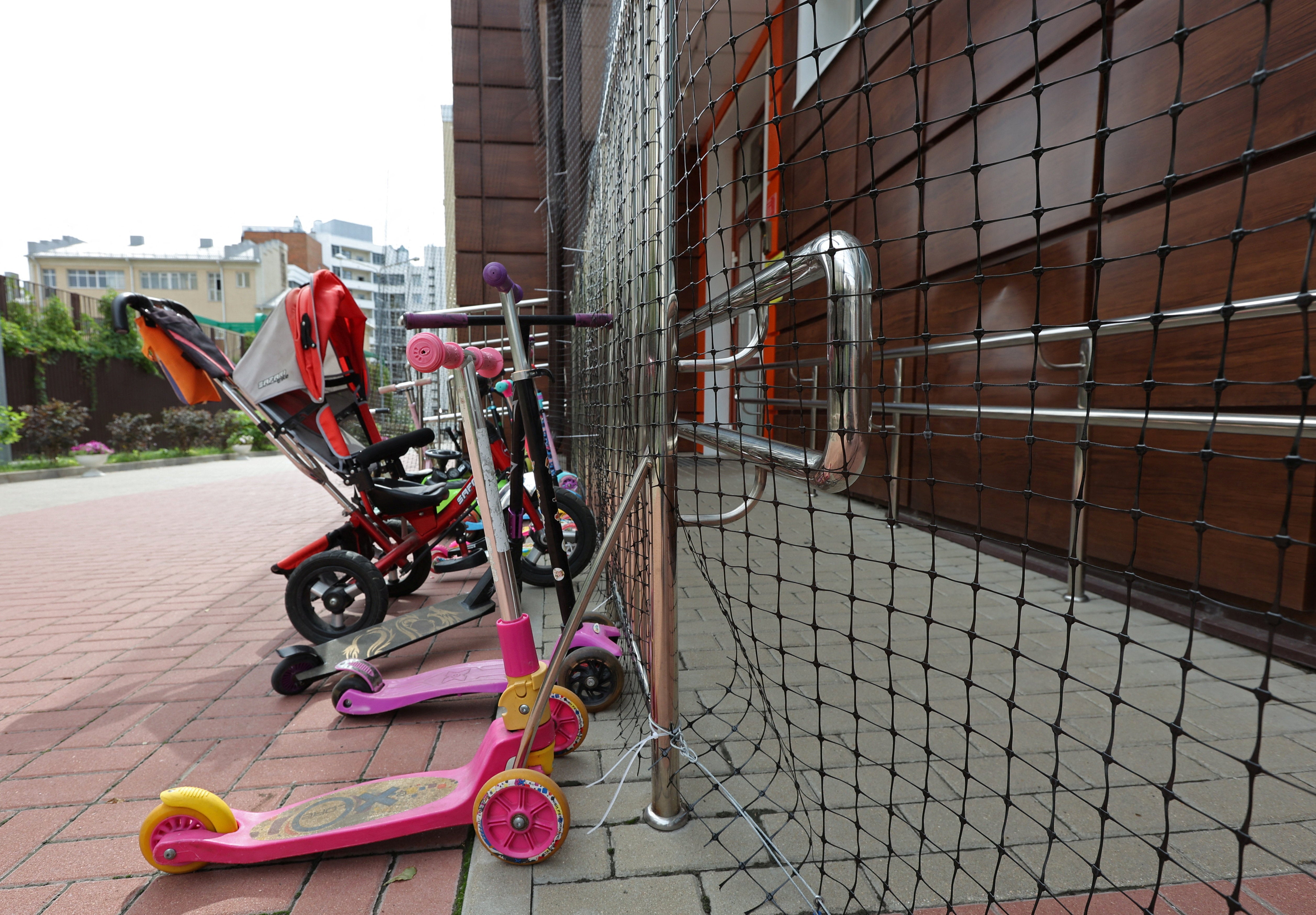 Bicycles and scooters are parked near a nursery, with netting installed