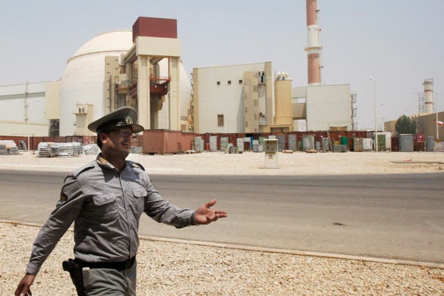 An Iranian security officer directs media at the Bushehr nuclear power plant, with the reactor building seen in the background, just outside the southern city of Bushehr, Iran (Vahid Salemi/AP)