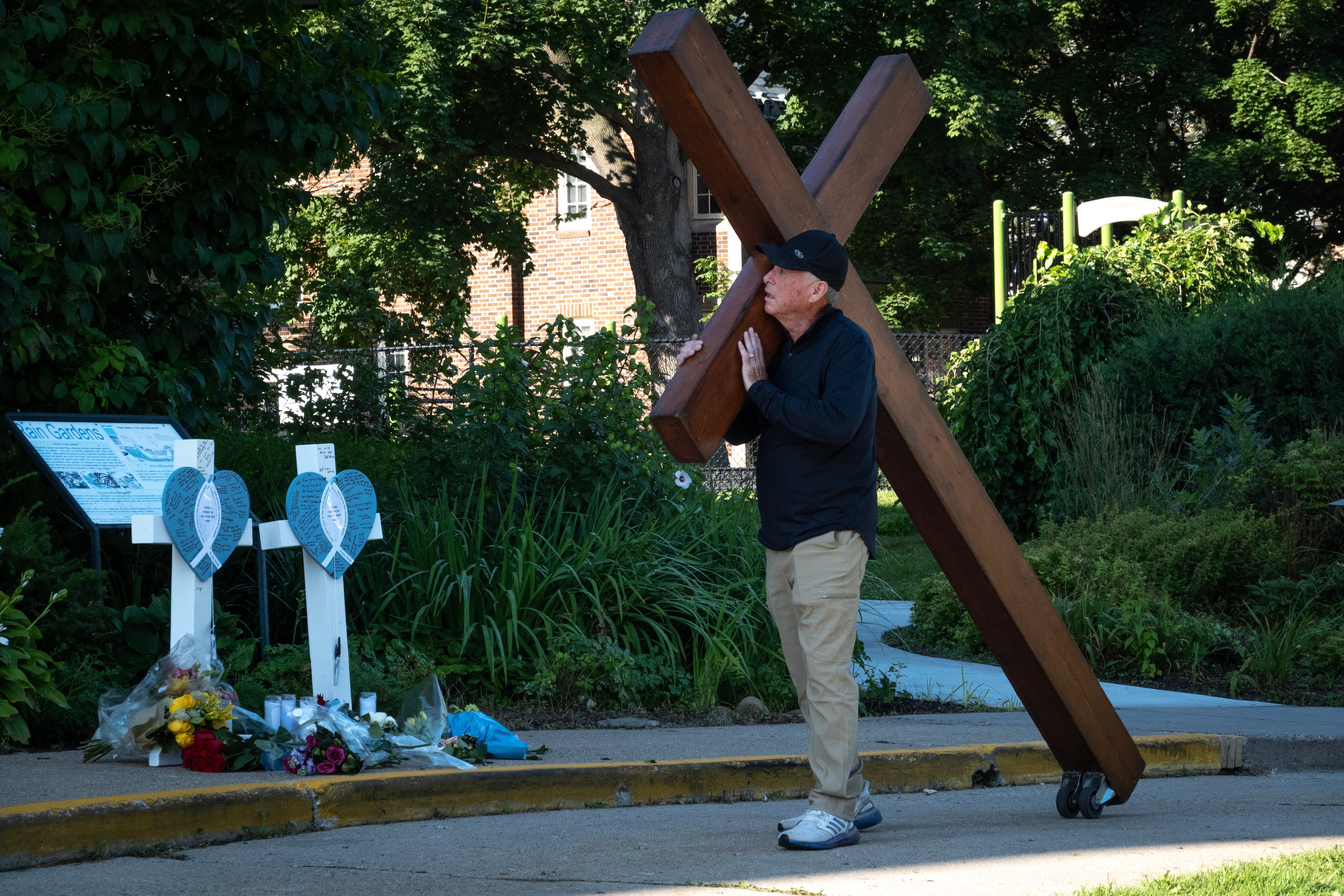 A man walks with a large wooden cross near the site of a mass shooting at a Catholic school in Minneapolis
