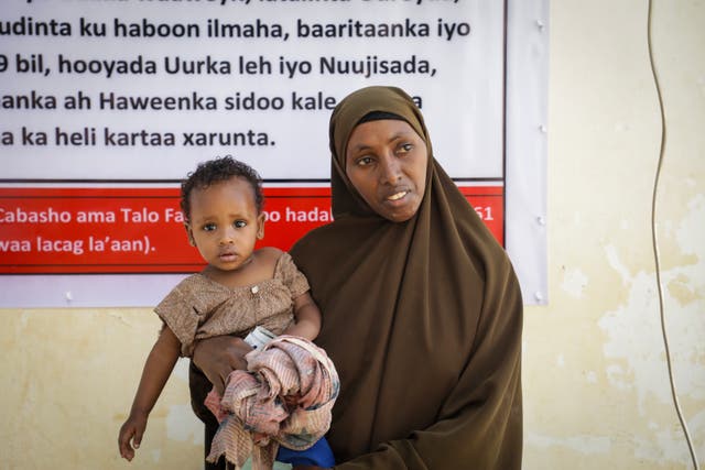 <p>Dahaboo, 38 stands for a portrait with her baby Aaden, one,  at a nutrition centre in Baidoa, Somalia. Nutrition centres such as this are under threat across Africa due to aid cuts</p>
