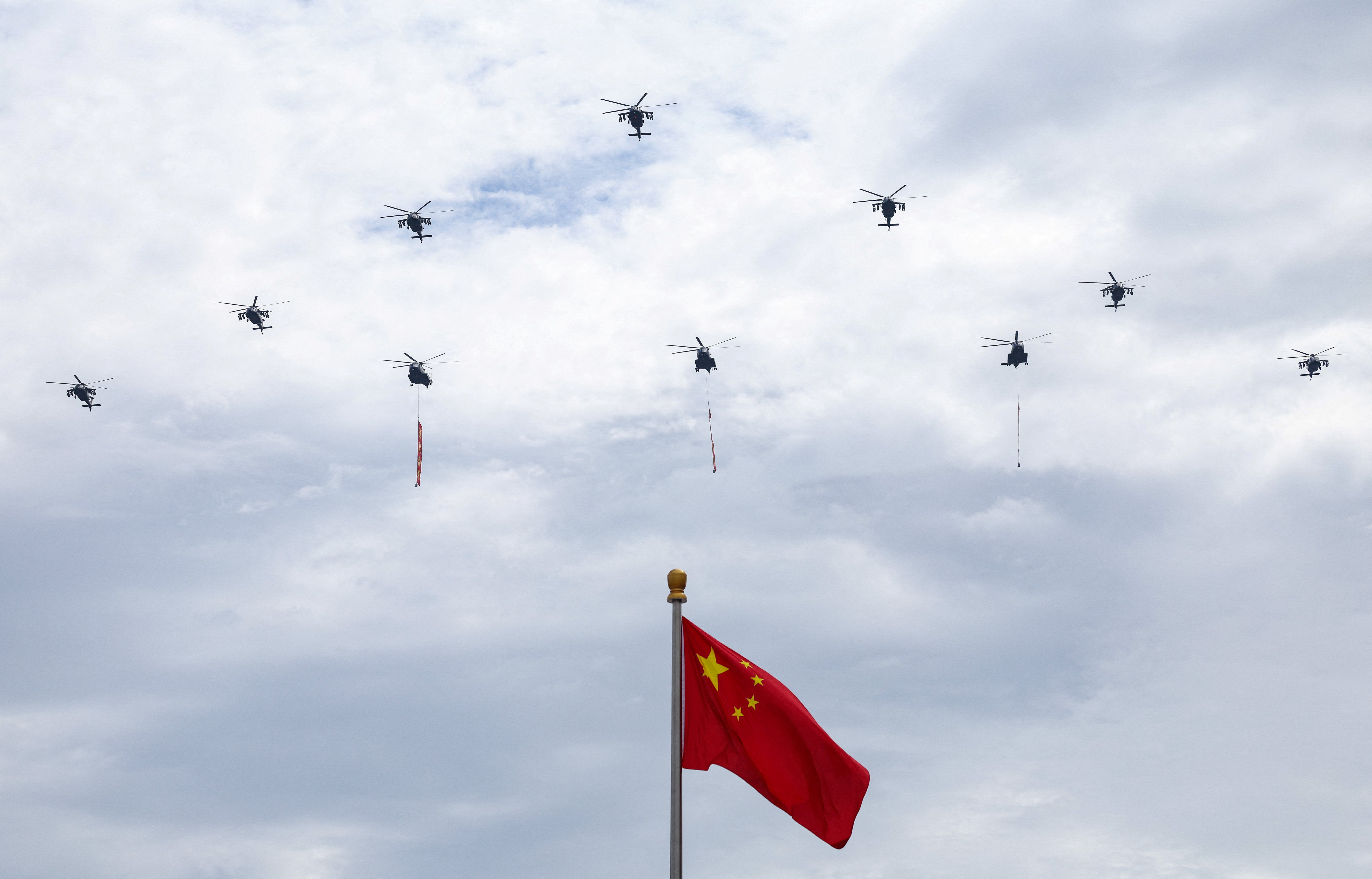 Military helicopters fly in formation past a Chinese national flag, during a flyover rehearsal ahead of a military parade