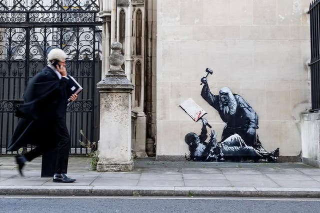 <p>A judge in a wig and gown beats an unarmed protester with a gavel in a new work by Banksy at the Royal Courts of Justice</p>