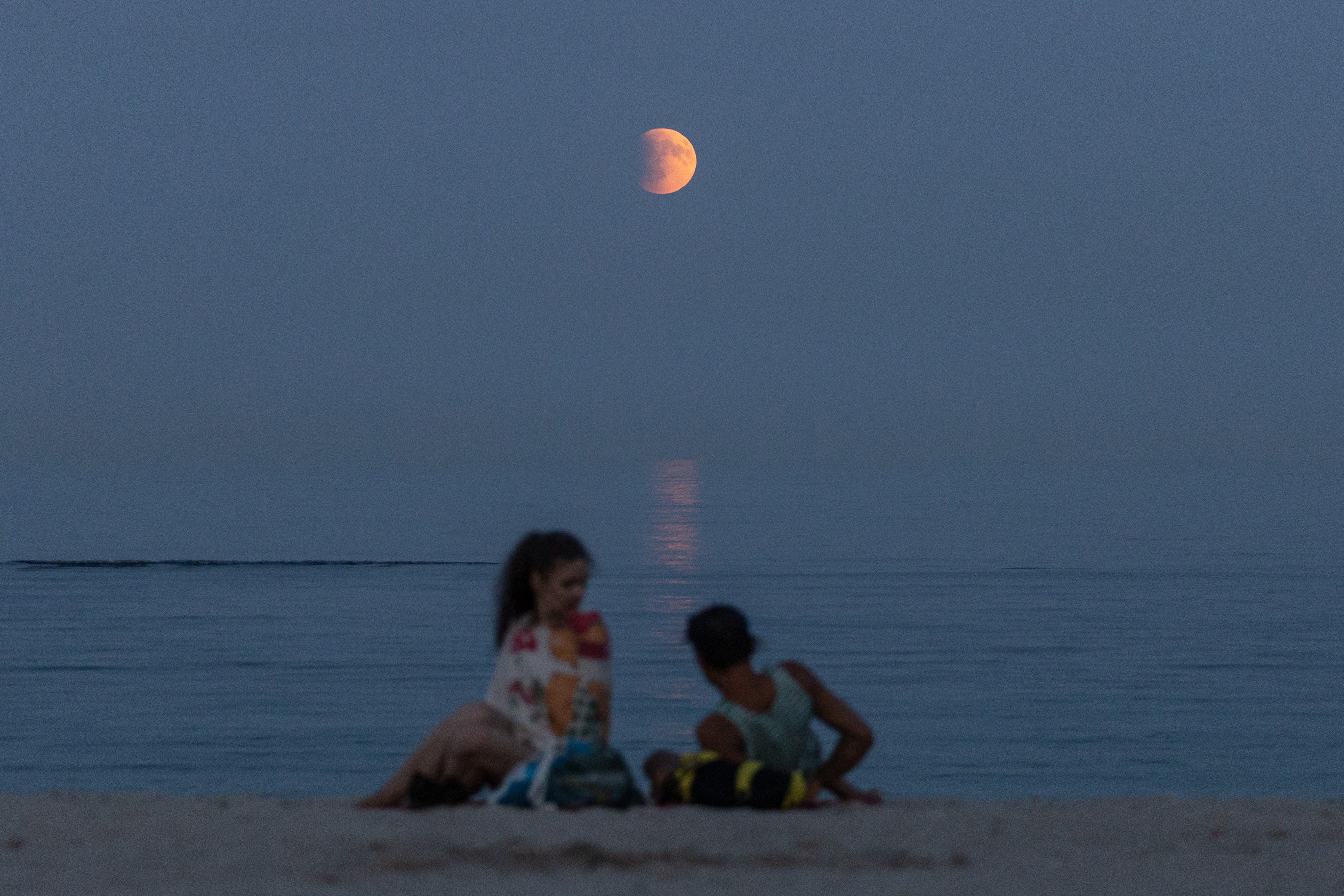 Beach-goers rest on a shore of the Black Sea with a full moon also known as 