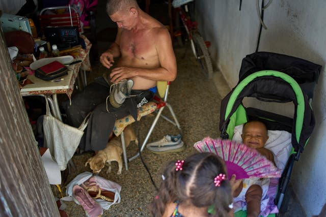 <p>A girl cools a baby off with a fan as a man repairs shoes during a blackout in Havana</p>