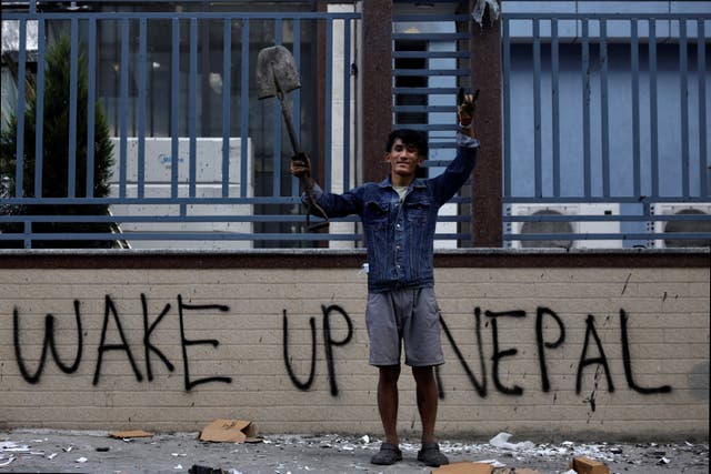 <p>A protester stands next to graffiti as he takes part in a cleaning campaign following violent protests in Kathmandu, Nepal</p>