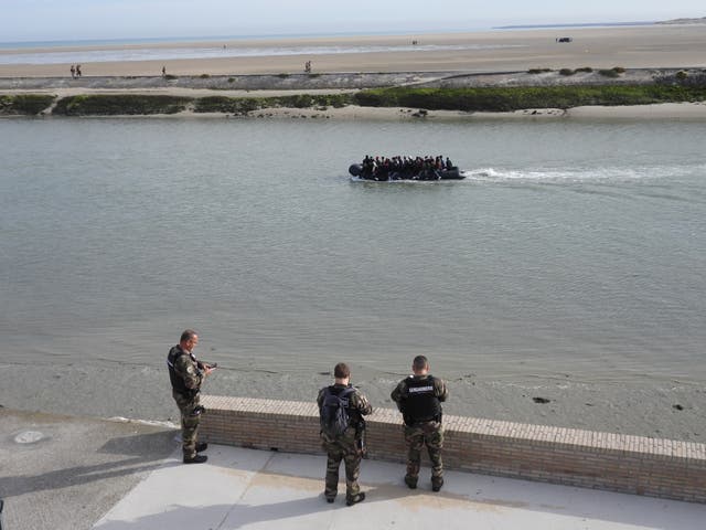 <p>French military reservists watch on as a boat of dozens of migrants begins the journey to the UK</p>