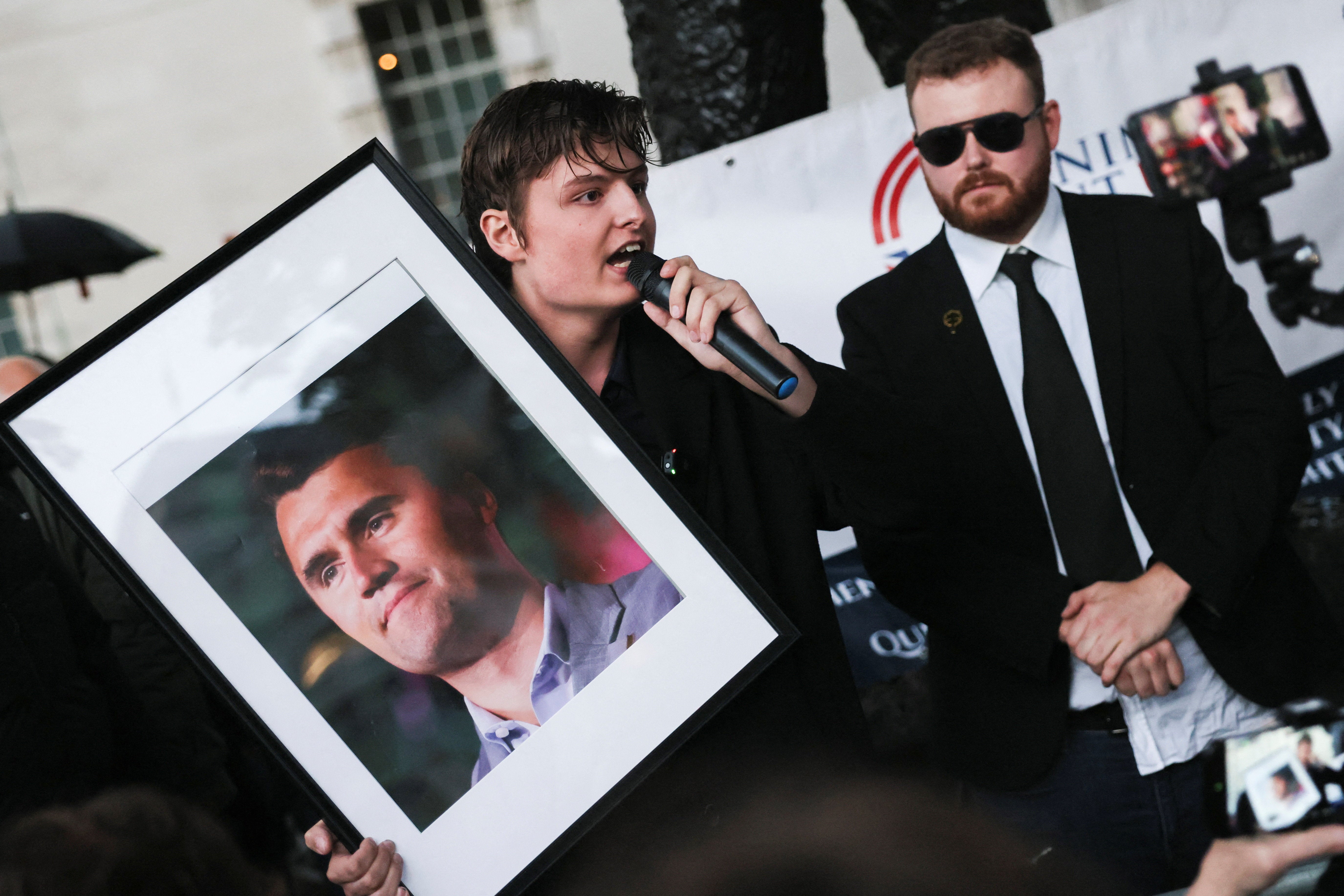 <p>A man holds a picture of Charlie Kirk while speaking next to Jack Ross, Chief Operations Officer for Turning Point UK, during a vigil at the Montgomery Statue in Whitehall</p>