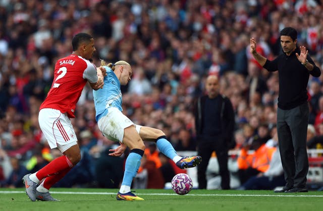 <p>Mikel Arteta watches on as William Saliba battles Erling Haaland for the ball</p>