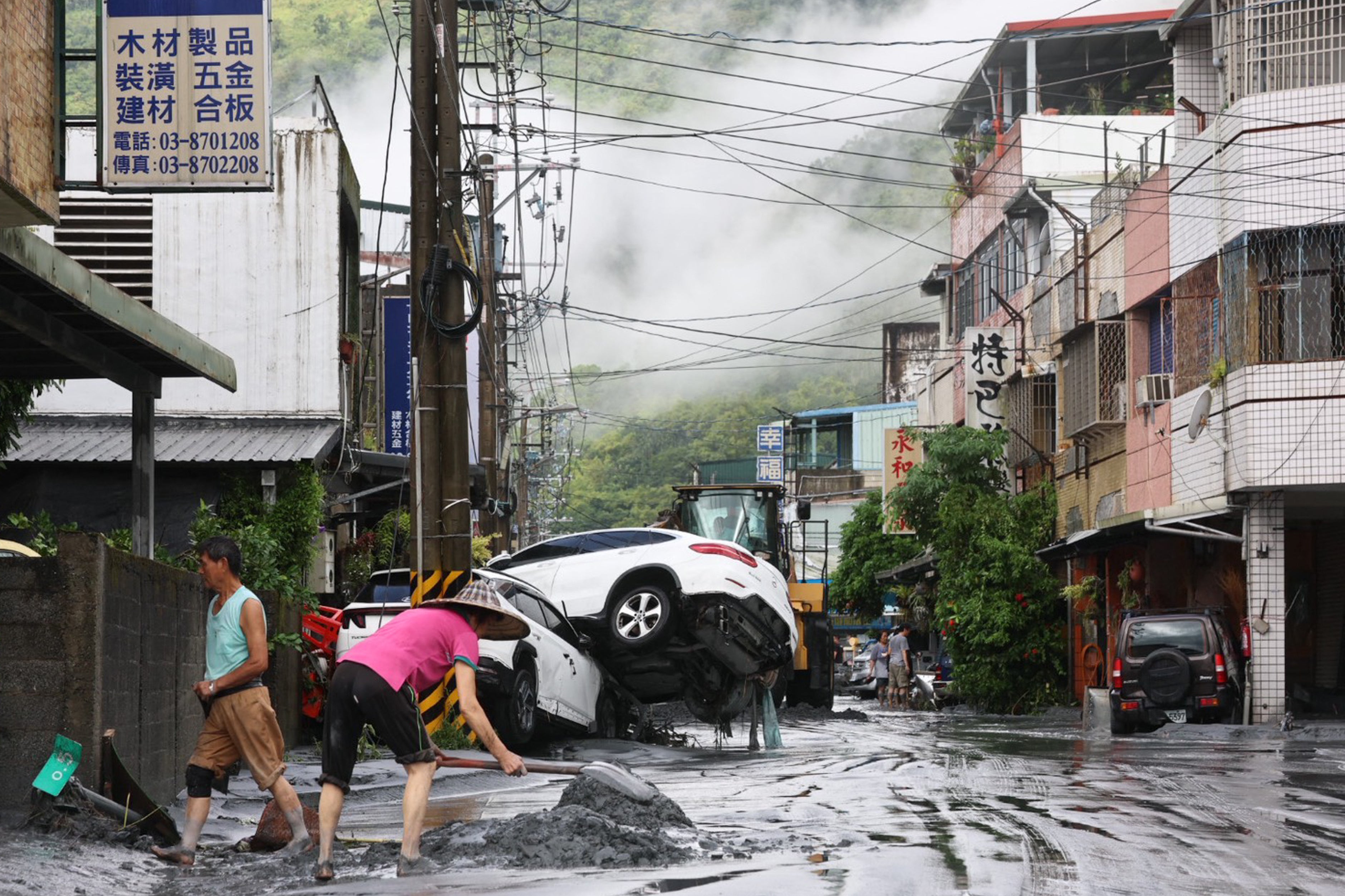 Residents clear mud from their property, while damaged cars are seen in the background, in Hualien
