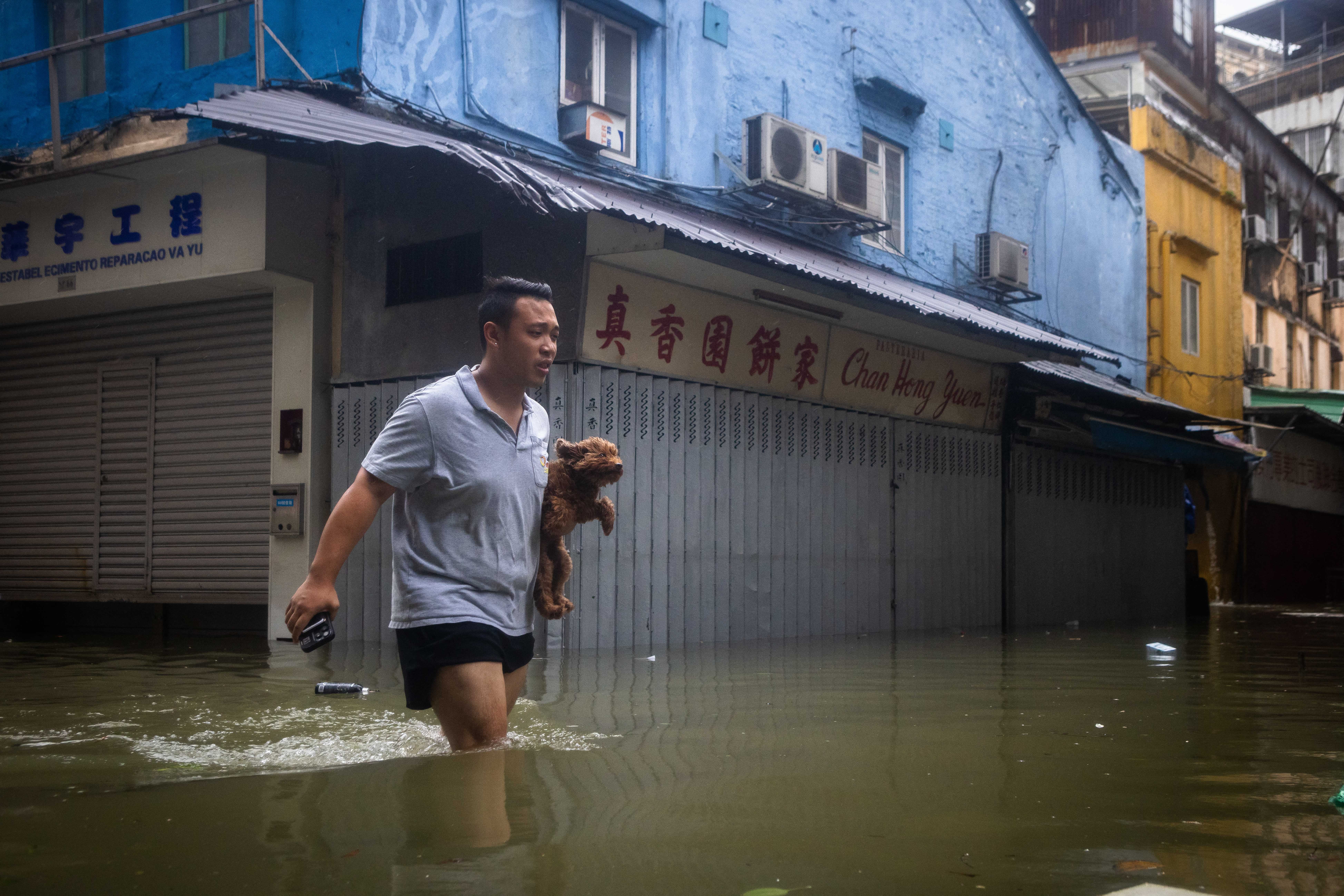 A man holds his dog while walking through a flooded street during the passage of Super Typhoon Ragasa in Macau on September 24, 2025