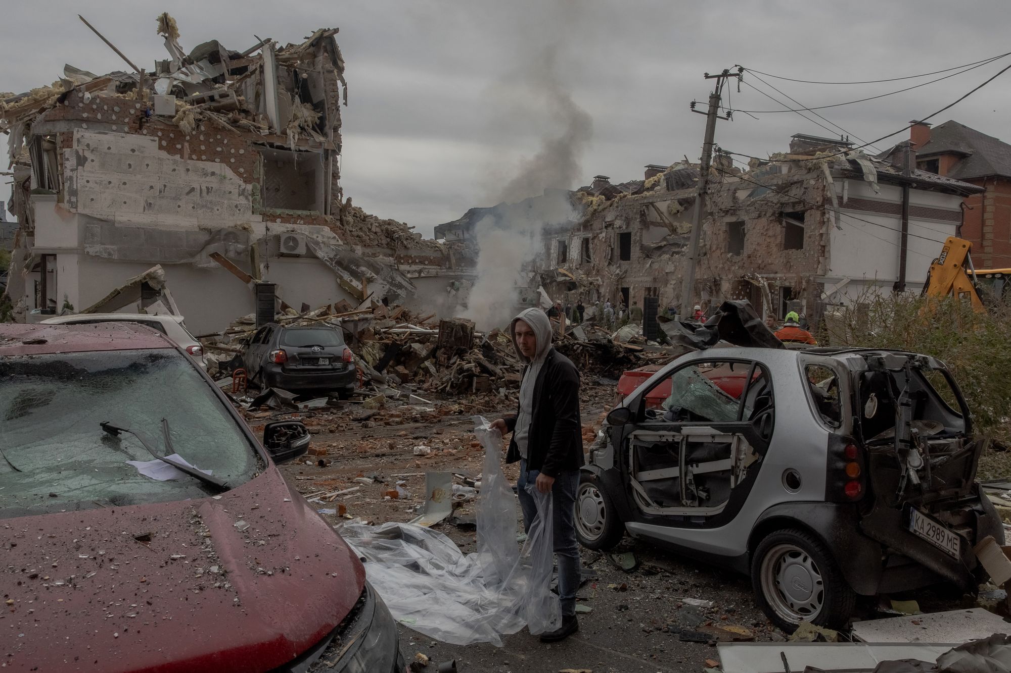 A man prepares to cover a damaged car with a plastic sheet at the site of heavily damaged residential buildings following a Russian air attack on the outskirts of Kyiv