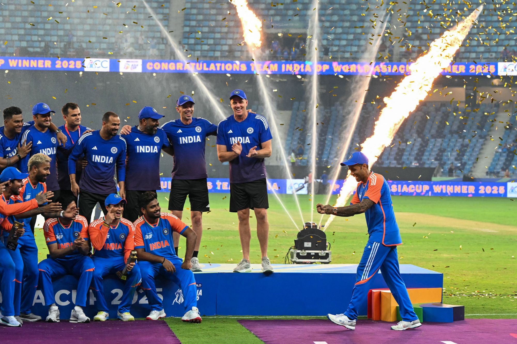 El capitán de la India, Suryakumar Yadav, correcto, finge mantener el trofeo mientras su equipo celebra su victoria de la Copa Asia