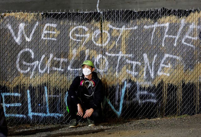 <p>A legal observer sits by a graffiti as people protest against the U.S. President Donald Trump administration's immigration policies, outside an ICE detention facility in Portland, Oregon, U.S., September 1, 2025</p>