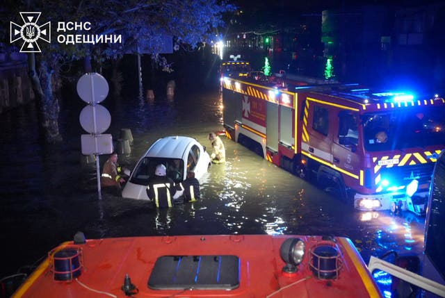 <p>Rescuers push a partially submerged car on a flooded street in Odesa</p>