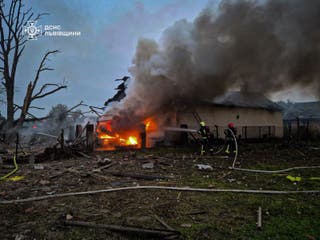 Firefighters extinguish a van on fire in a backyard of a residential house damaged during morning Russian drone and missile strikes in Lviv region