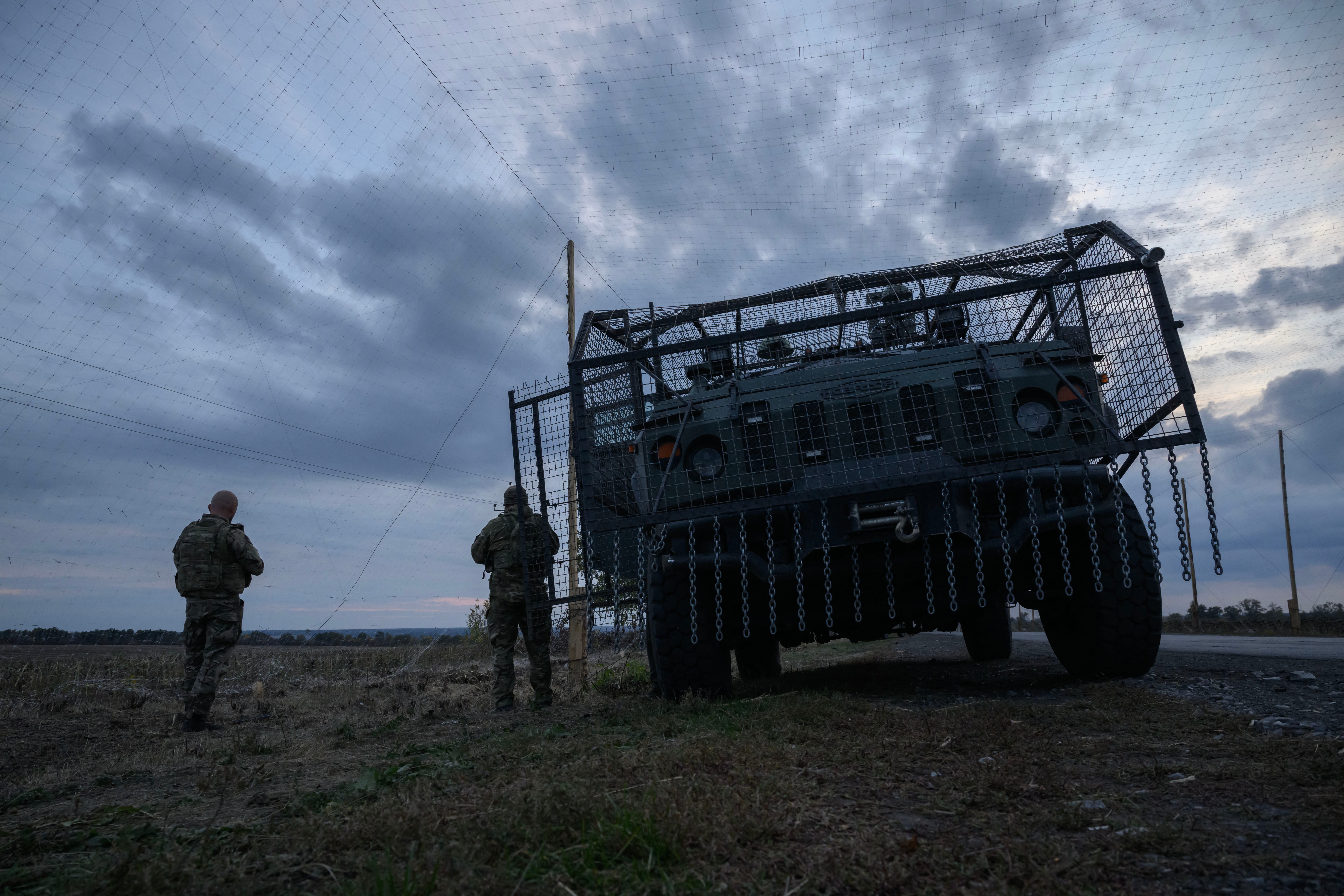 Ukrainian soldiers stand in front of an armored military vehicle surrounded by a cage to protect against drone strikes on a road near Oleksandriyuka, October 6, 2025.